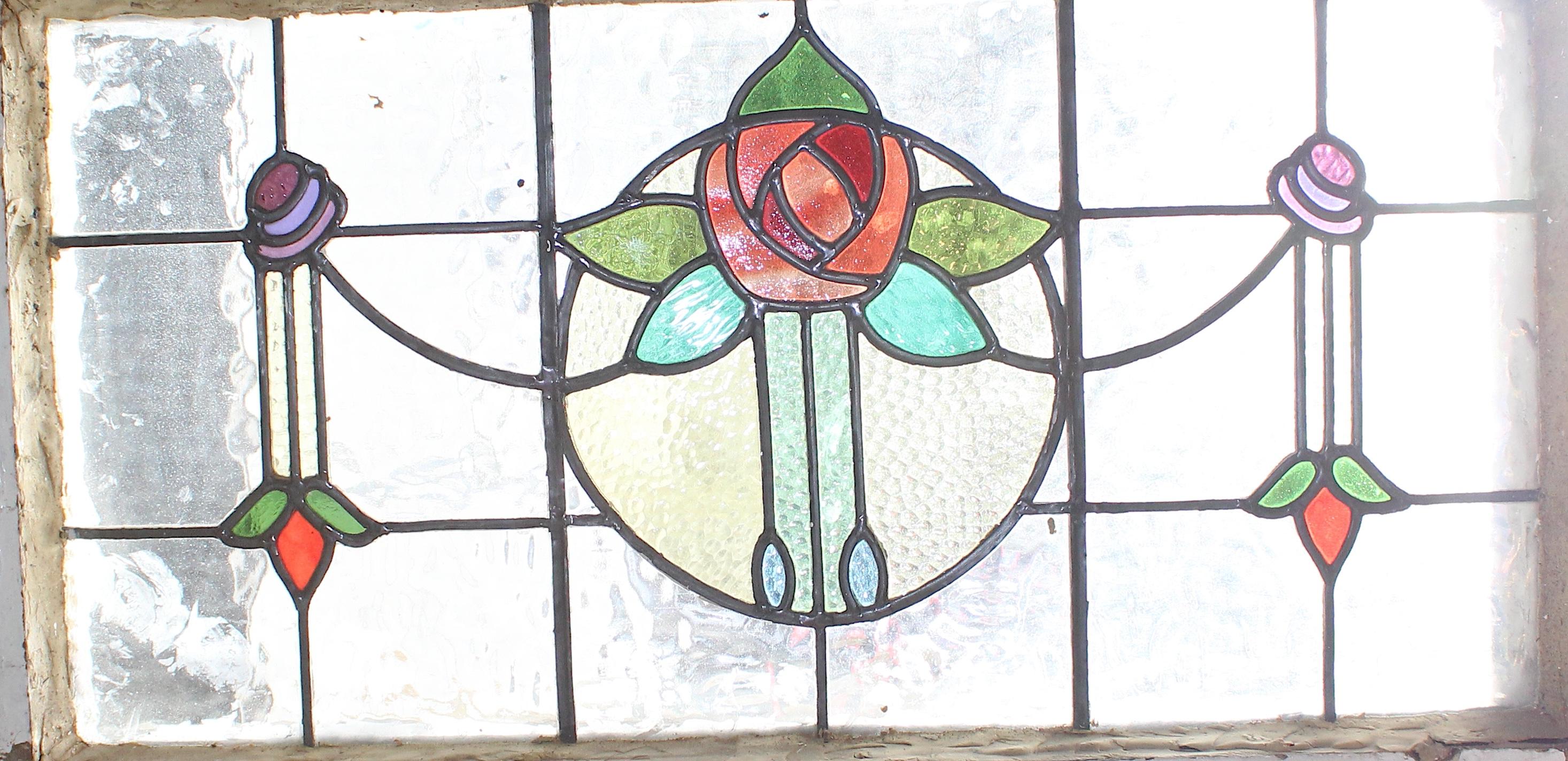 Fenêtre ancienne en verre clair texturé pour préserver l'intimité, avec des motifs de vitraux dans un style déco. Le rosier central est une belle pièce maîtresse avec des pédales rouge vif et des feuilles vertes.
Actuellement dans un cadre en bois -