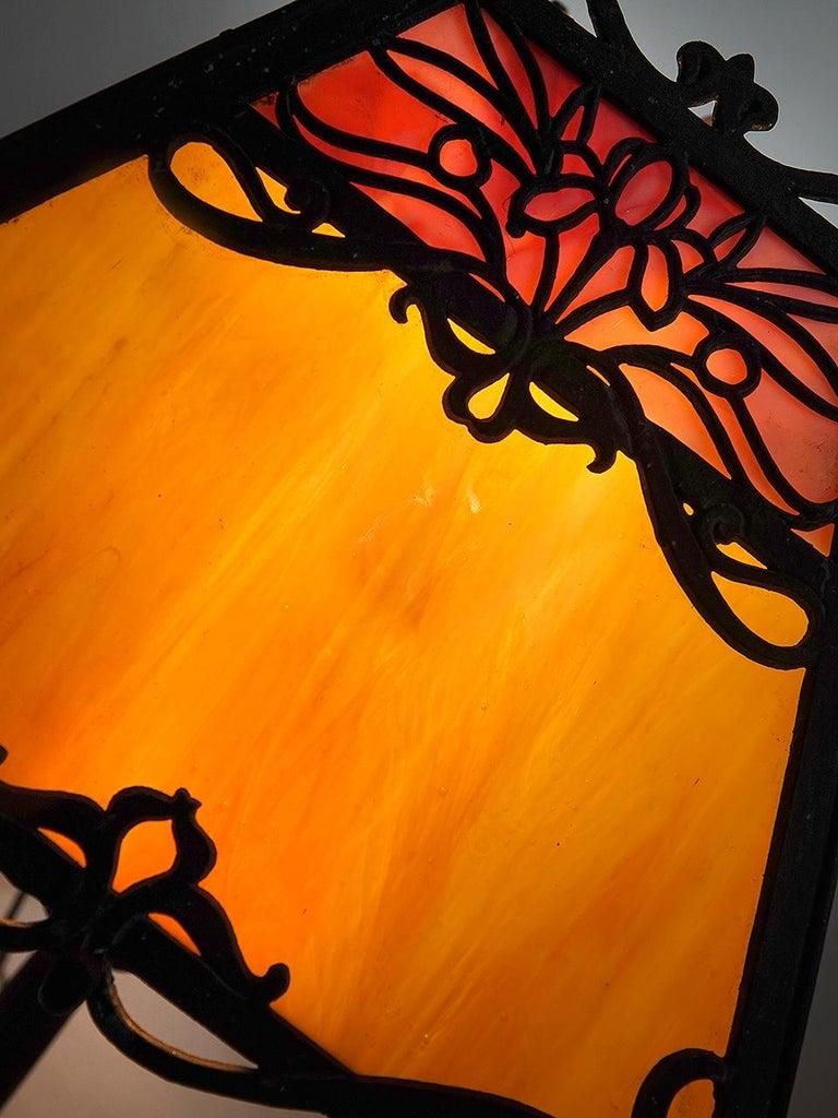 This is a nicely designed Arts and Crafts table lamp. It simple and clean with a tented shape and cast floral filigree panels. Each panel has two pieces of complimentary colored glass. The size makes 11 x 20 inch size makes it perfect as a bedside