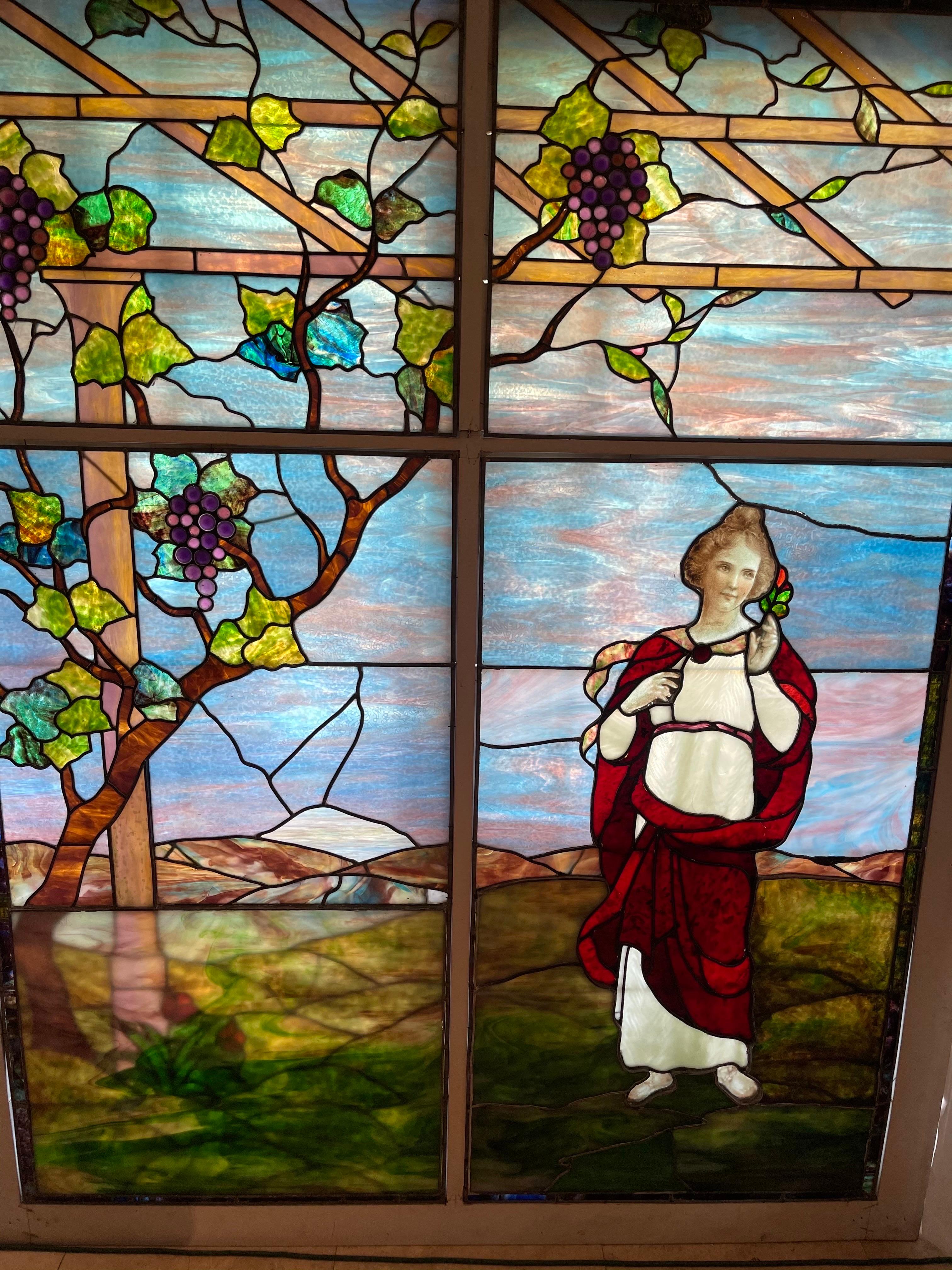 A tiffany type stained glass window depicting a woman standing in the mist of a grape arbor, in the foreground executed with early lead came molded glass grapes 
And a nicely painted face 


Over the past 50 years, we have been collecting