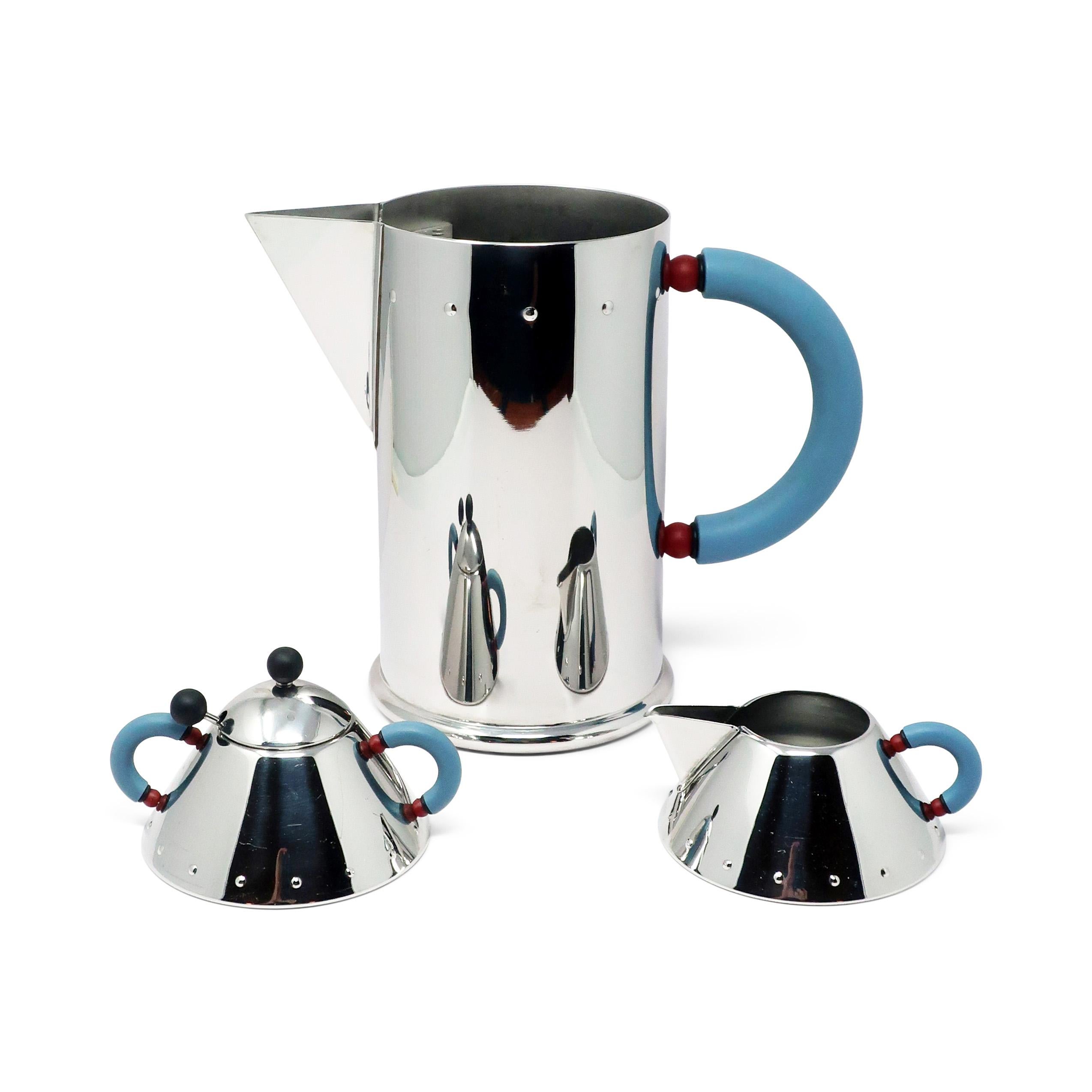 A stainless steel sugar bowl and creamer set, along with a water pitcher, designed by Memphis Group pioneer Michael Graves for Alessi of Italy. Sugar bowl and creamer in polished 18/10 stainless steel with blue-grey plastic handles and tiny maroon