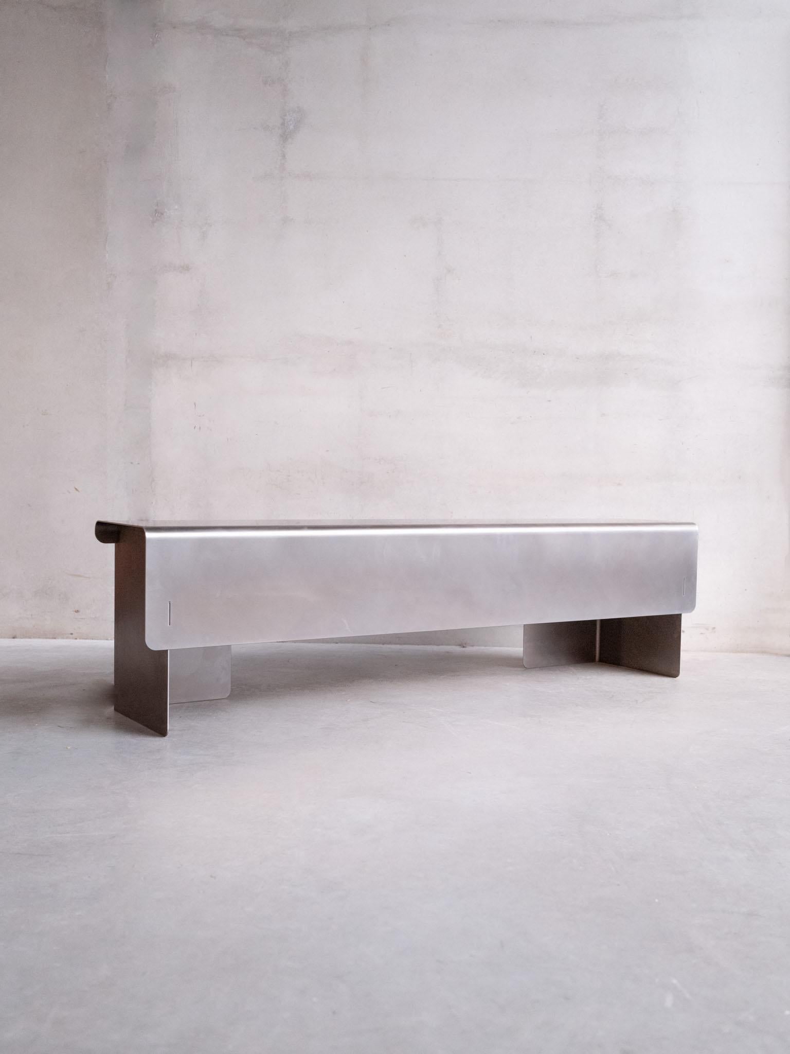 Este banco de acero inoxidable de la diseñadora belga Rebecca Ackaert traslada su filosofía de diseño arquitectónico a un formato más grande y comunitario. Mide 45 cm de alto, 160 cm de ancho y 35 cm de profundidad, y conserva la claridad y