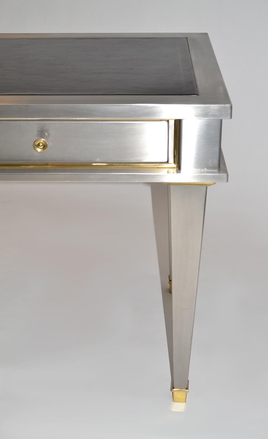 Stainless steel bronze neoclassical revival desk 20th century (mid-) after John Vesey. A diminutive steel writing table, desk or bureau plat after a design by John Vesey. Clad in brushed steel with gilt bronze accents and handles, the desk features