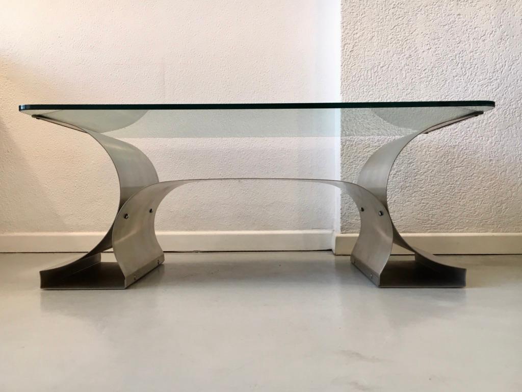 Brushed stainless steel base and clear glass top coffee table by François Monnet, produced by Kappa, France, circa 1970s.

Most of the furniture created by François Monnet feature entire steel sheets that are bent or curved, therefore, these pieces