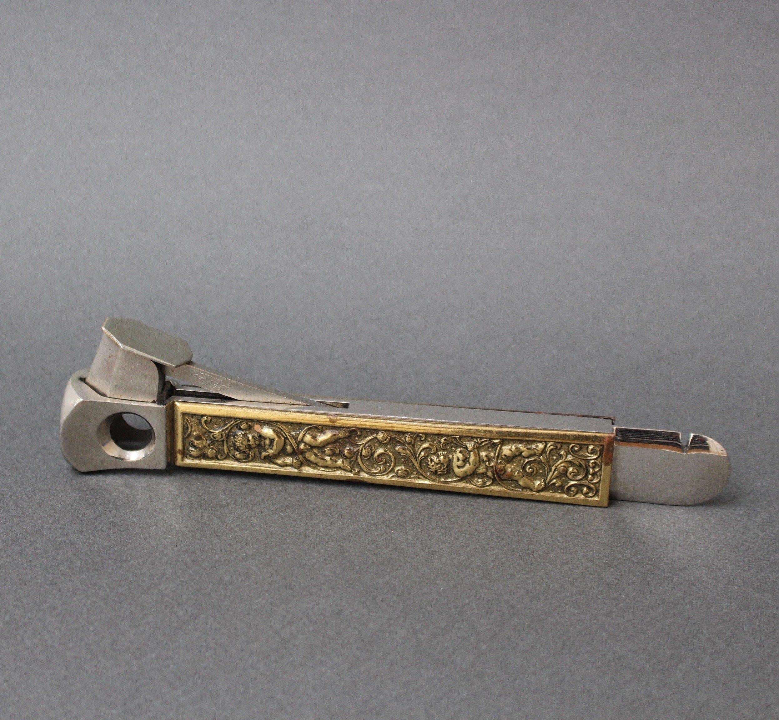 Stainless steel vintage German cigar cutter from Donatus Solingen (circa 1950s). Decorated on the sides with brass relief depicting cherubs and flourishes. Wonderfully charming however, more useful today as a decorative desktop conversation piece