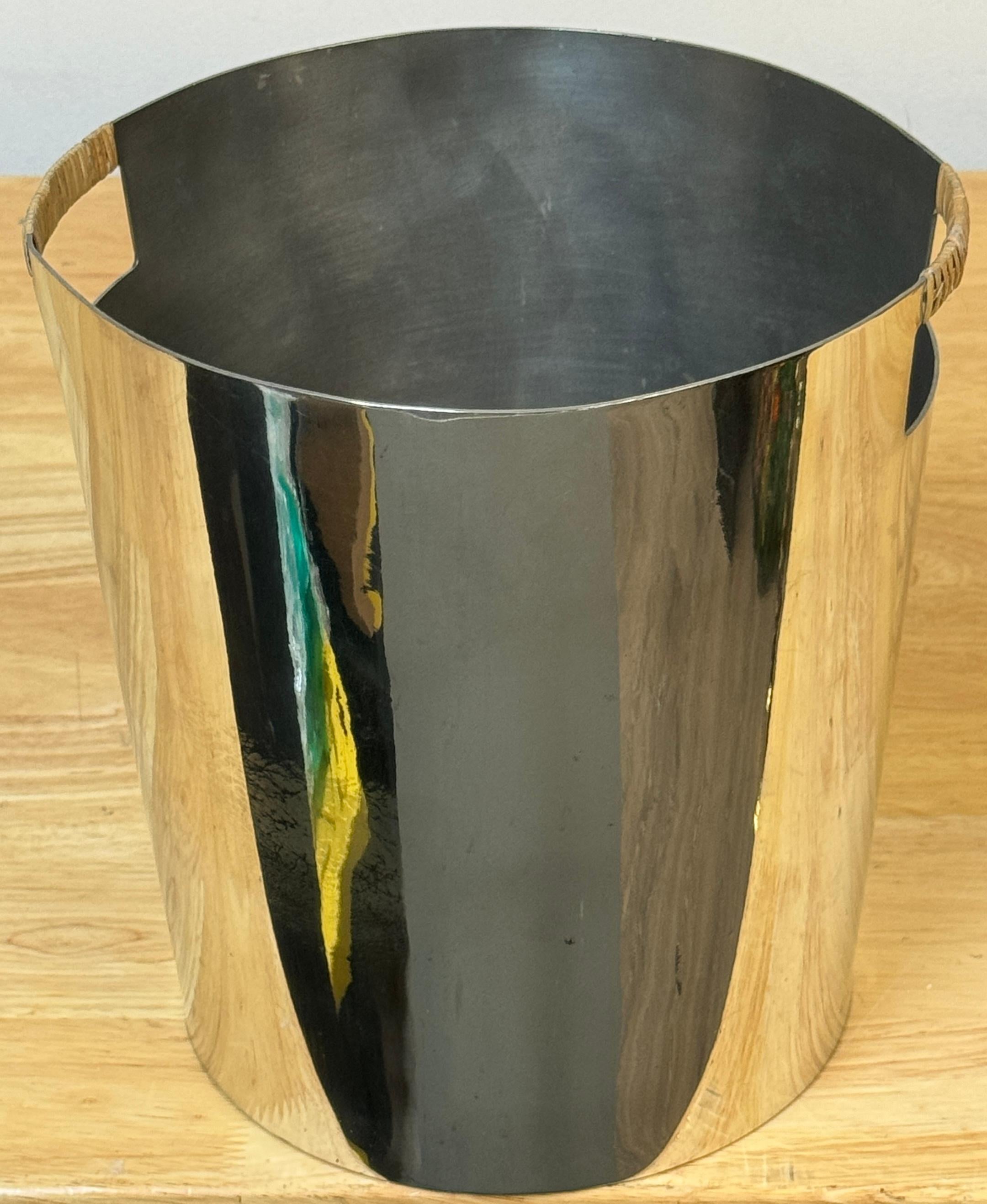 Stainless Steel and Rattan Wastepaper/TTrash Can by Waterworks, 1992

This sleek and modern wastepaper basket stands 9 inches high and has a 9.5-inch diameter. The polished stainless steel body is complemented by twin rattan-wrapped handles, adding