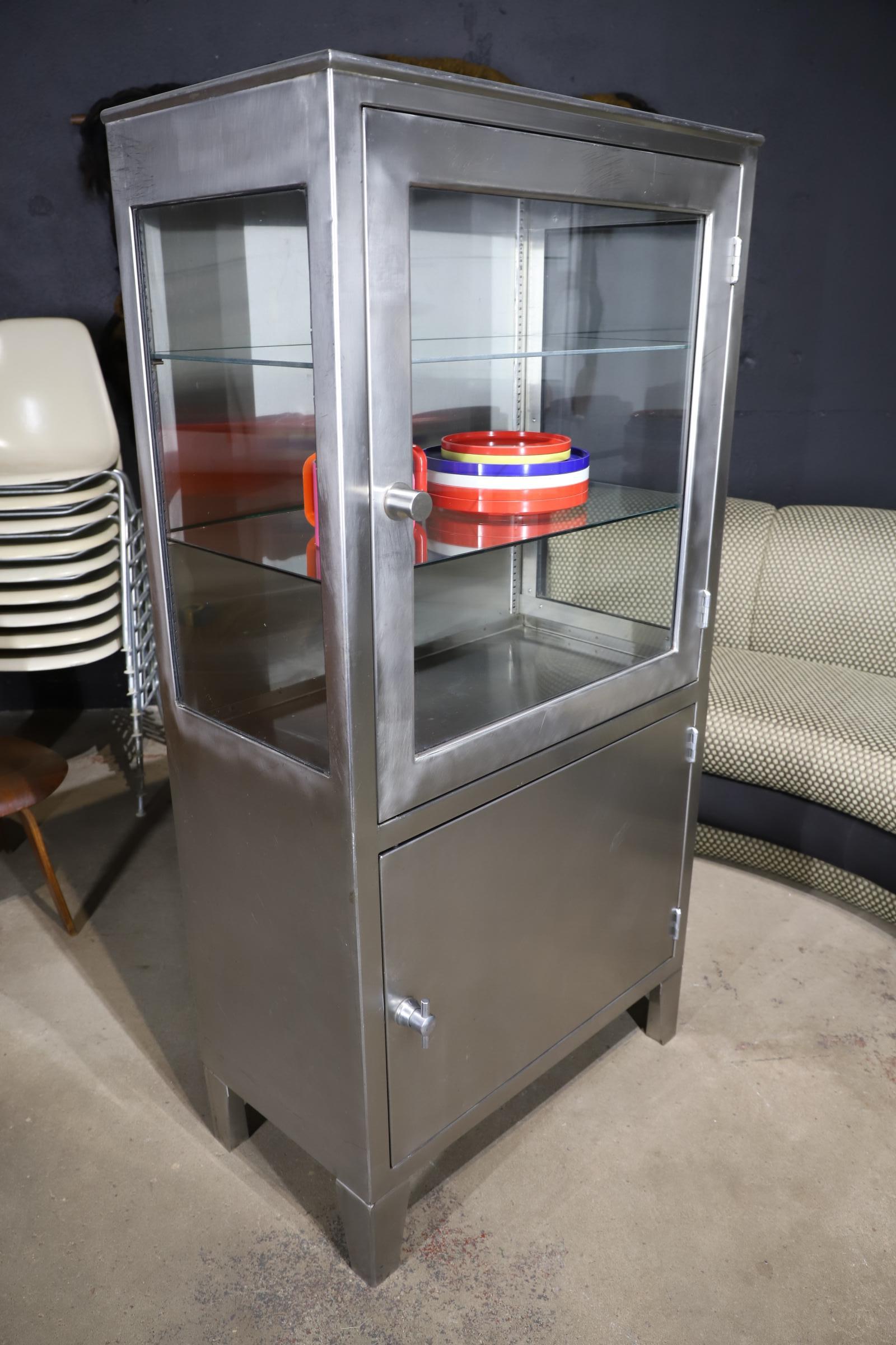 Unique uses of vintage industrial stainless steel medical cabinet are endless, kitchen storage, a bar, to extra storage for the bathroom. Display glass top section with two glass shelves (more could be added if needed) and lower cabinet with