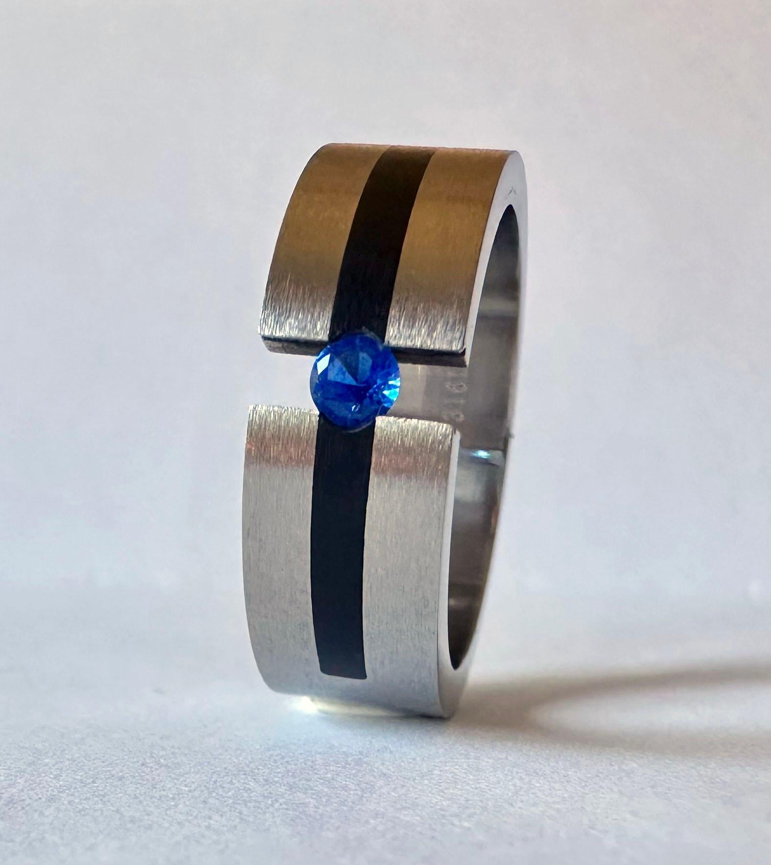 This stainless steel tension ring holds a lovely blue round 0.23 carat sapphire in space bay its sides 