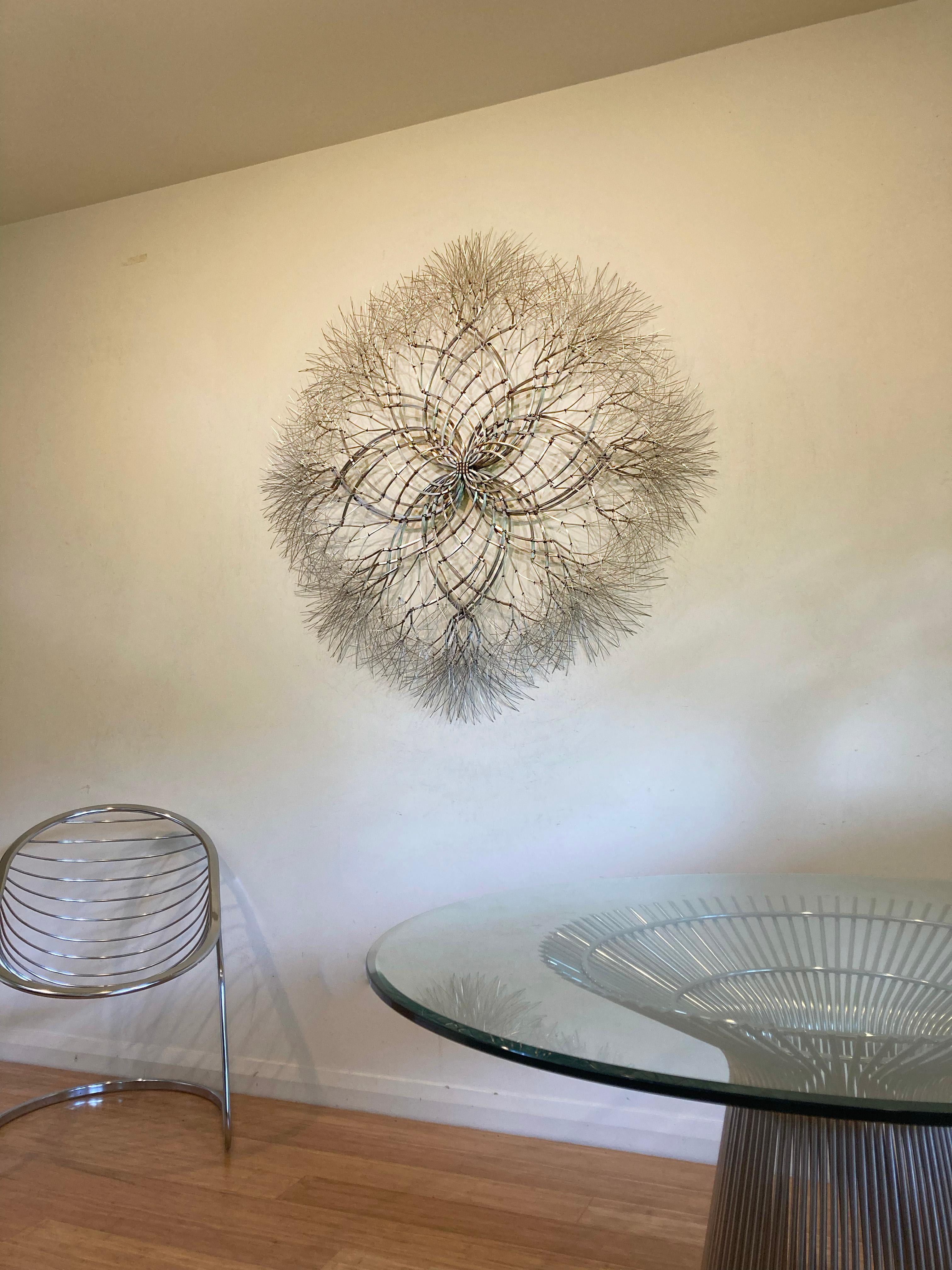 Stainless steel. 

Kue King created this starburst sculpture using stainless steel wire. The polished stainless steel gives the sculpture a shine, reflectivity, and mirrored finish that adds sparkle to the room and picks up on colors that surround