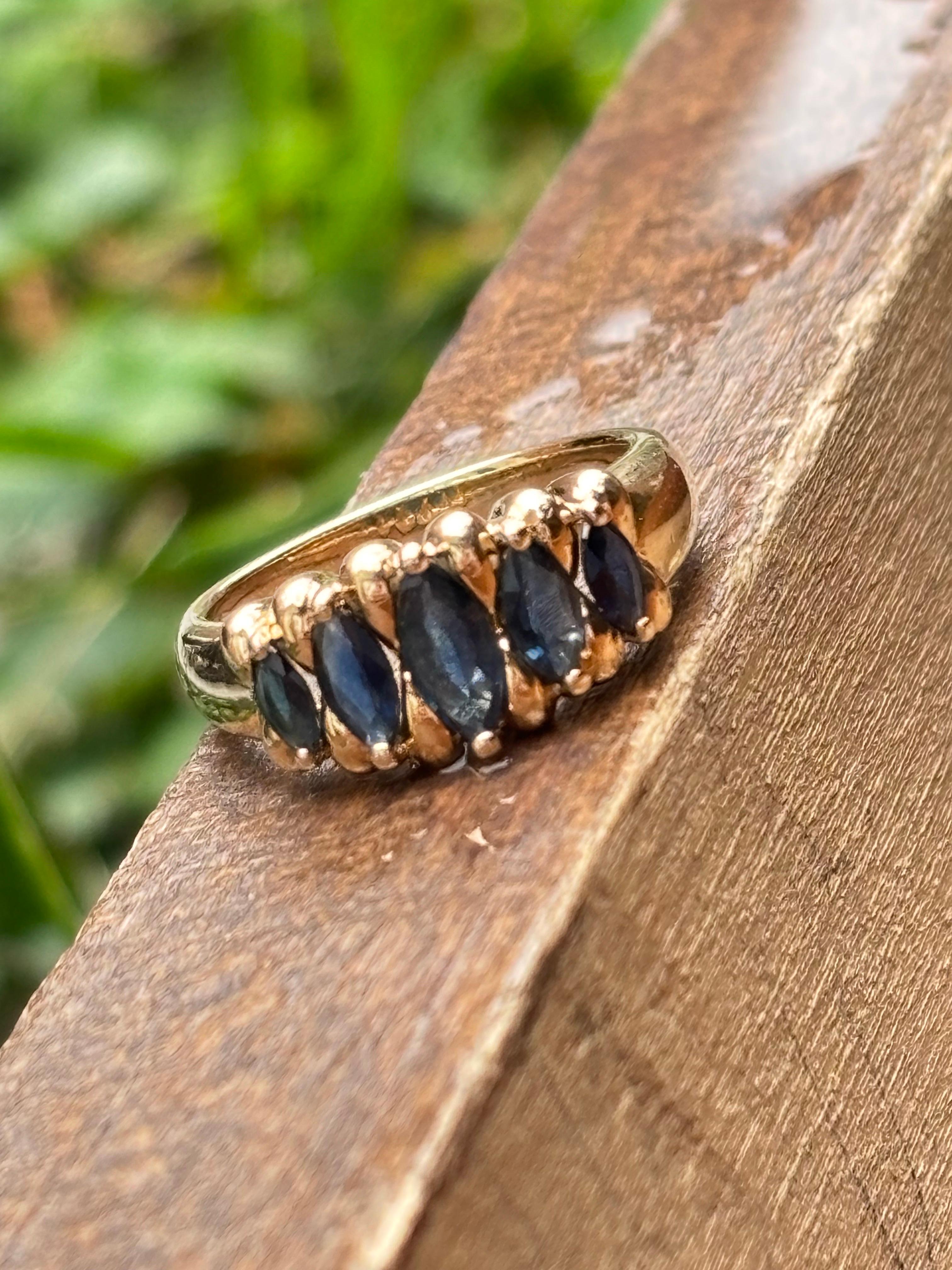 Cette élégante bague vintage des années 1980 est fabriquée en or jaune 14k lumineux et conçue avec une monture en escalier intemporelle. Les cinq saphirs bleus naturels taille marquise totalisant environ 1,20 carat affichent une riche couleur bleue