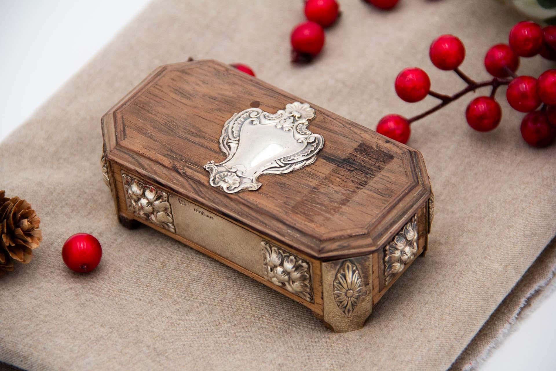 Description: Stamp box in rosewood with raised silver applications and resting on four feet. Metal: Silver. Origin: Portuguese. Brand: javali II Title. Weight: 148.09 grams. Dimensions: 4.2cmx11.1cm. Content: 833/1000. Assay Mark: Yes, between 1887