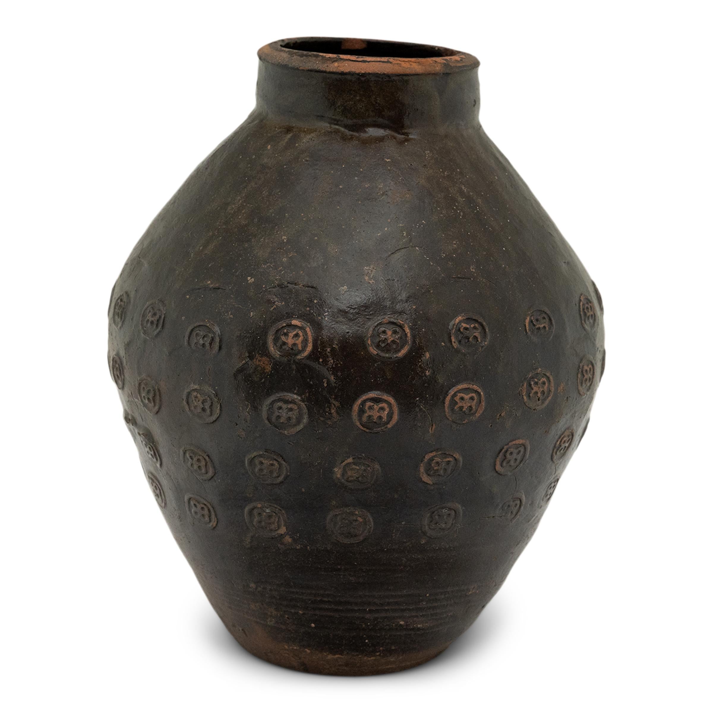 This unique 19th century Chinese earthenware pot is distinguished by its remarkable stamp pattern. With a brown drip glaze, this vase features a bulbous shaped body that stands on a flat unglazed base. The round body tapers to a constricted neck,
