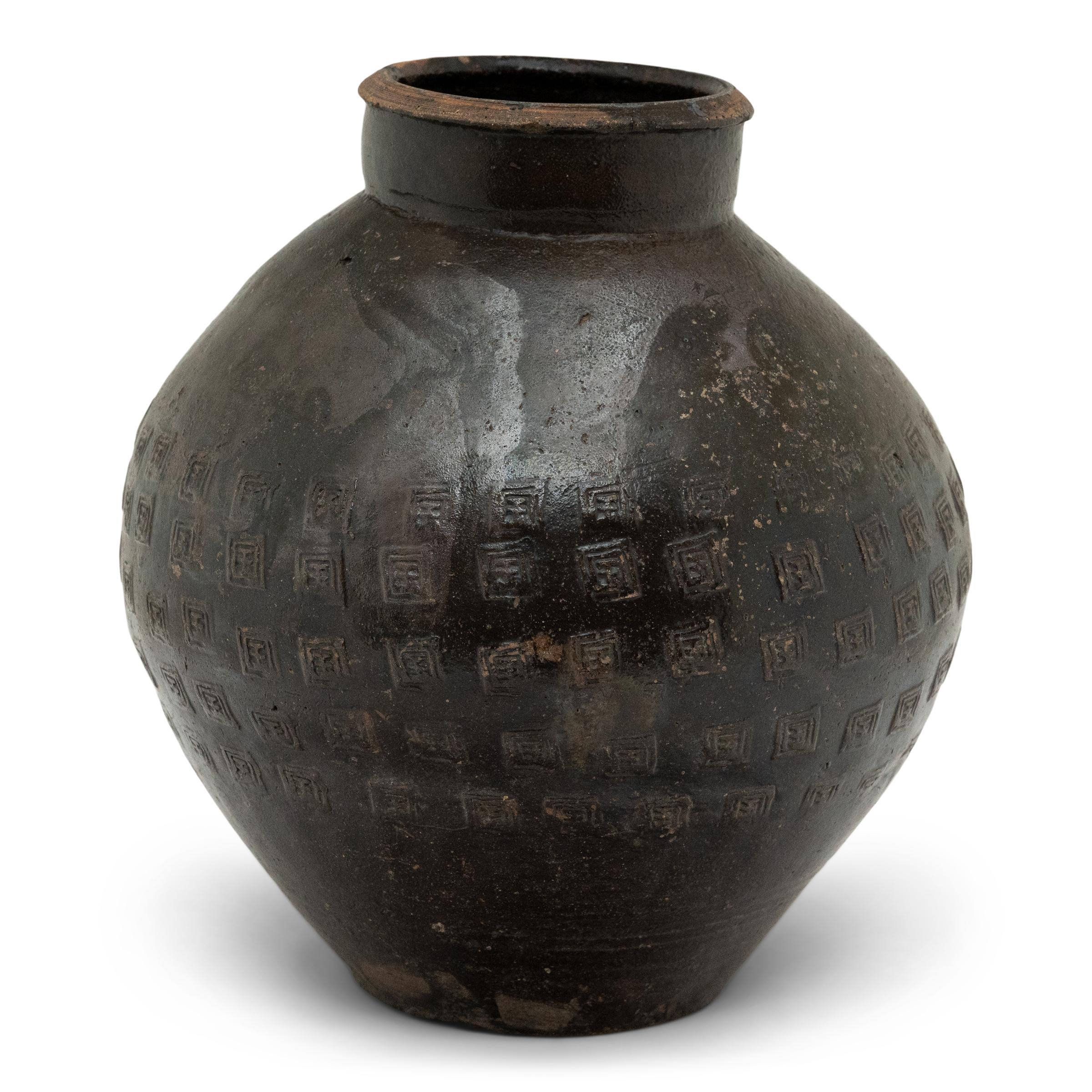 This unique 19th century Chinese earthenware pot is distinguished by its remarkable stamp pattern. With a brown drip glaze, this vase features a bulbous shaped body that stands on a flat unglazed base. The round body tapers to a constricted neck,