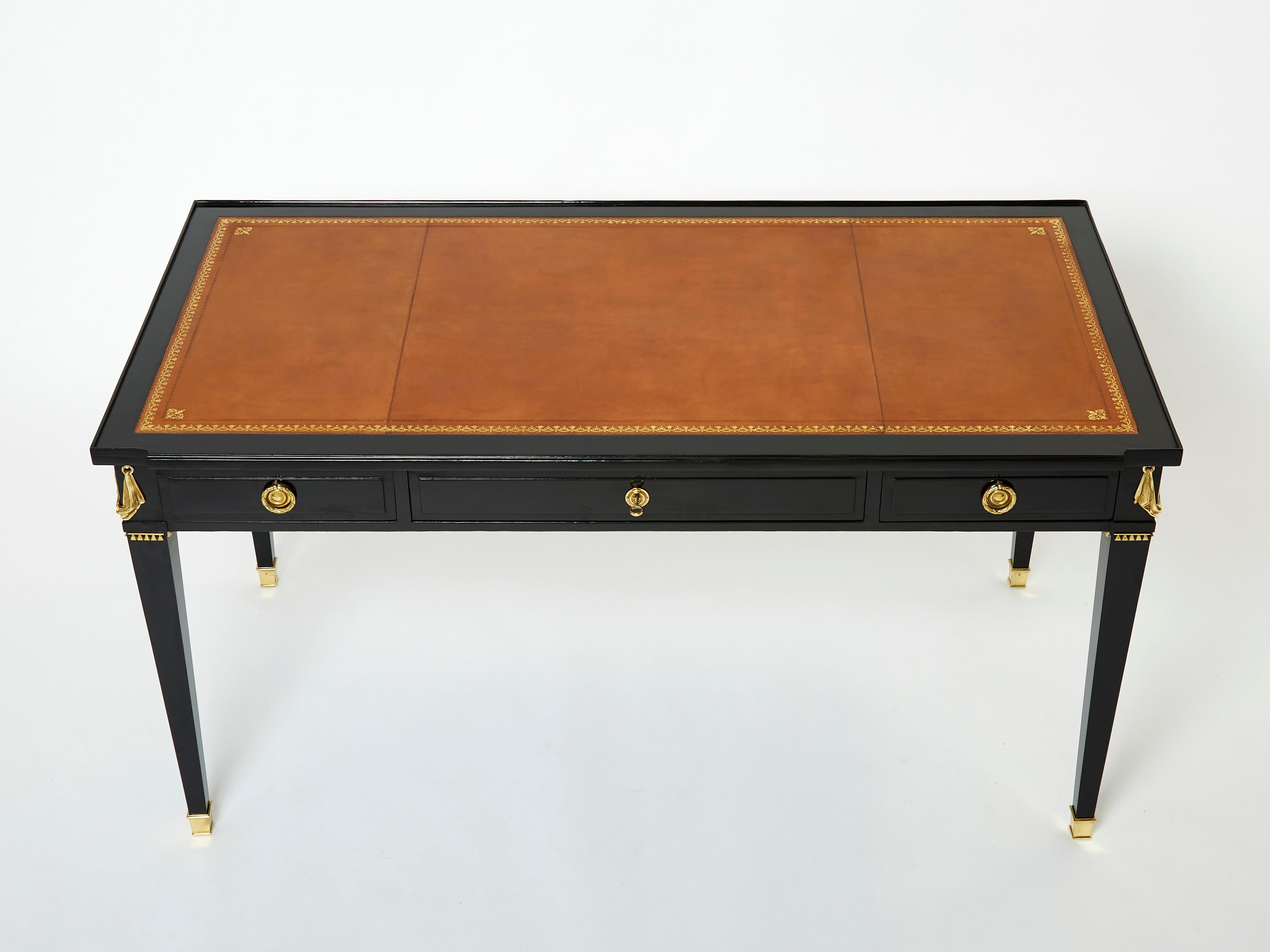 This rare Louis XVI style ebonized desk stamped Maison Jansen has been made in the early 1950s with black varnished mahogany wood, cognac leather top, and rich gilt bronze decor and accents. With its sleek rectangular bureau plat shape, fluted feet
