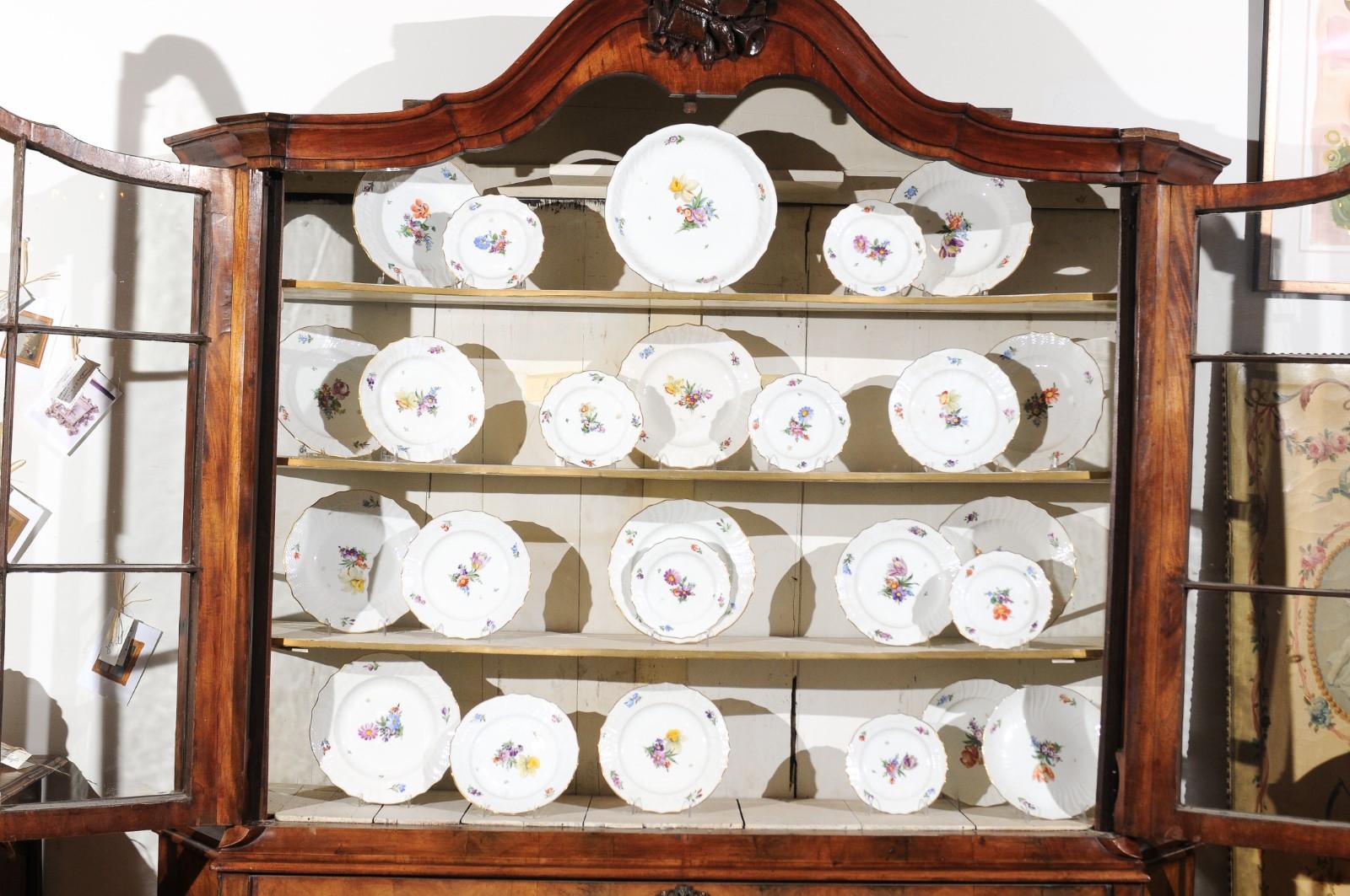 A set of 64 hand painted stamped Royal Copenhagen china from the early 20th century, with multi-color floral décor and scalloped gilt trim. Born in Denmark during the first half of the 20th century, this 16-piece place setting and serving dishes