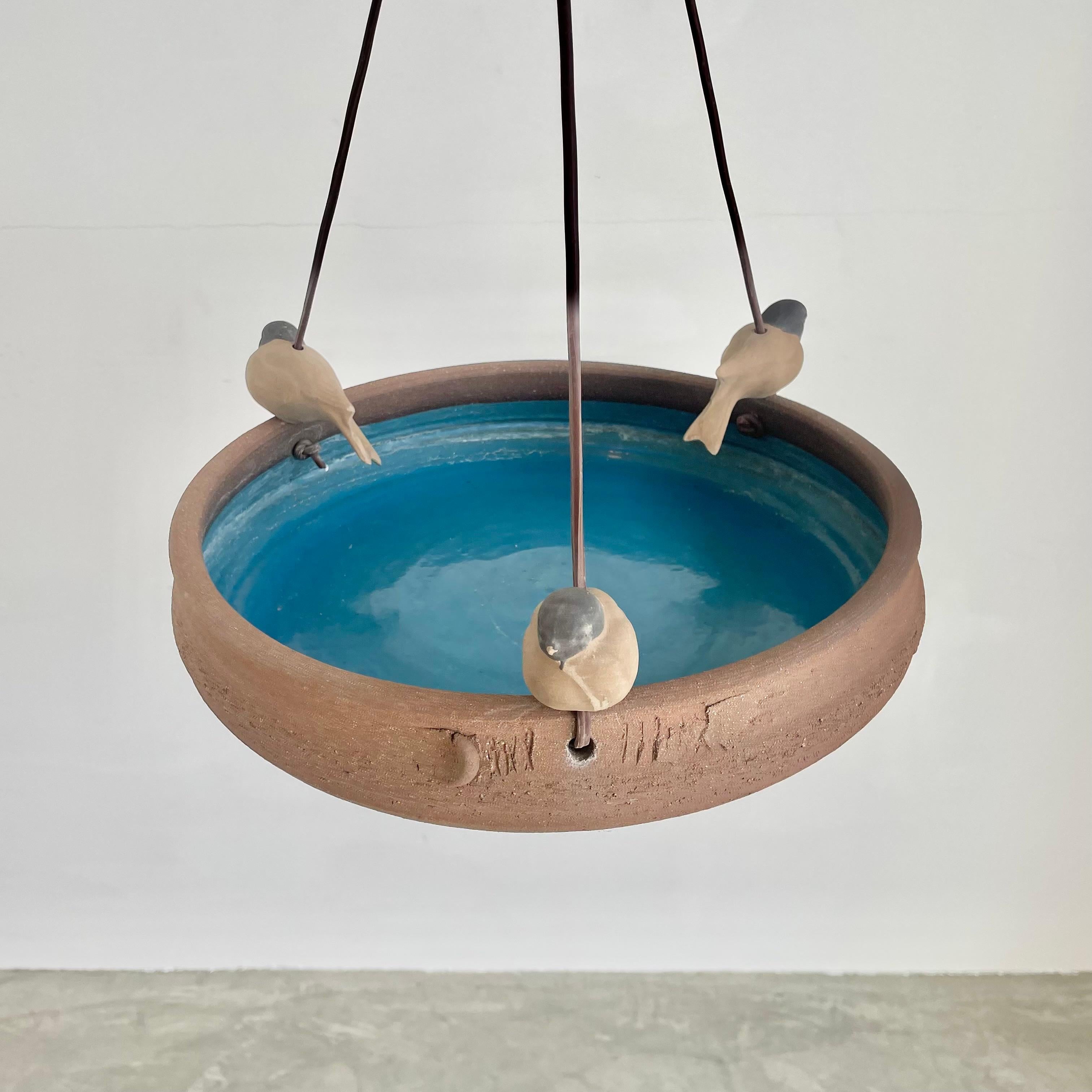 Beautiful hanging bird bath by noted Californian ceramicist, Stan Bitters. Plastic cords are attached at three points on the dish and meet in a clay disk at the middle of the cords. Each plastic cord is adorned with a clay ball and a cast clay bird