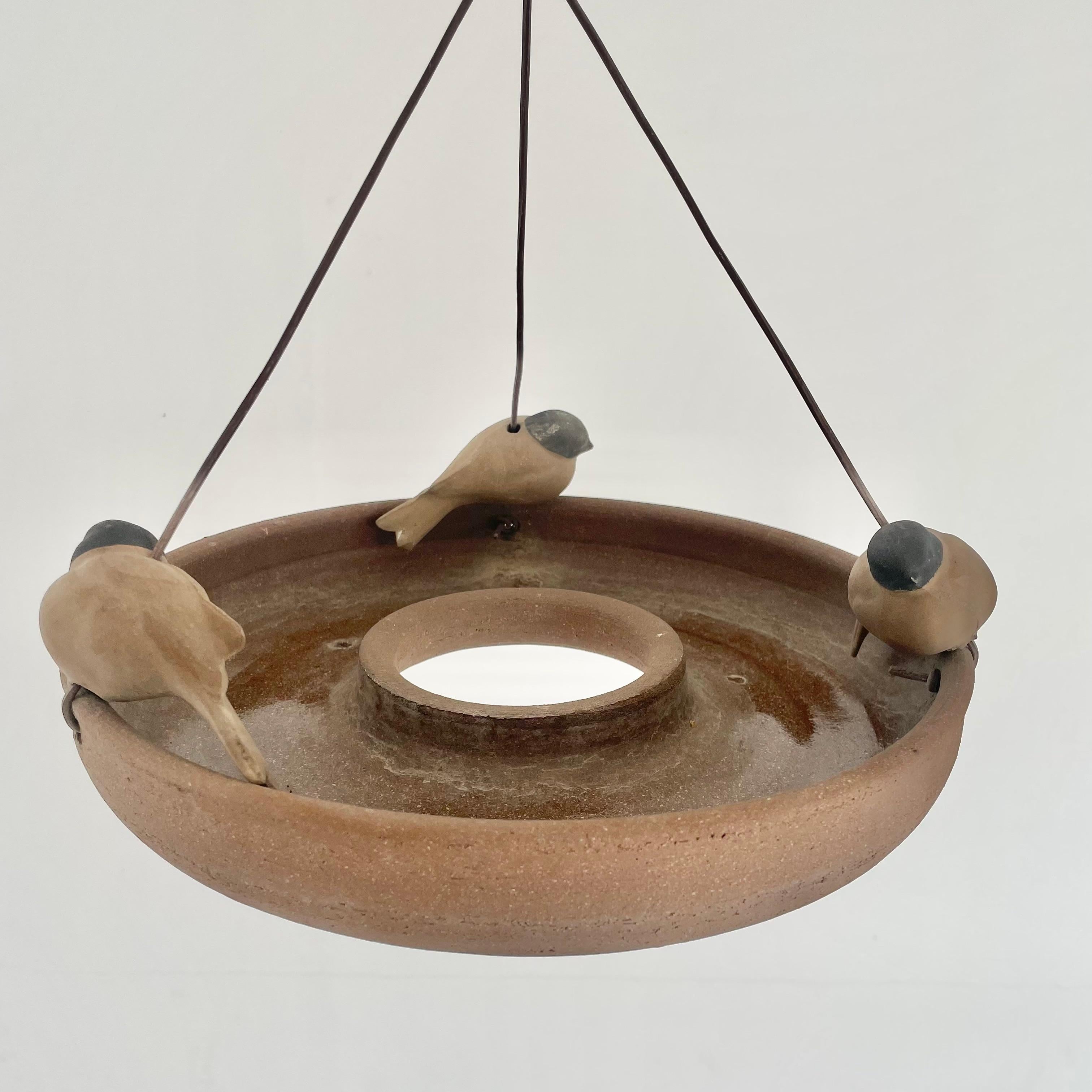 Beautiful hanging bird feeder by noted Californian ceramicist, Stan Bitters. Plastic cords are attached at three points on the dish and meet in a knot at the middle of the cords. Each plastic cord is adorned with a cast clay bird at their base.