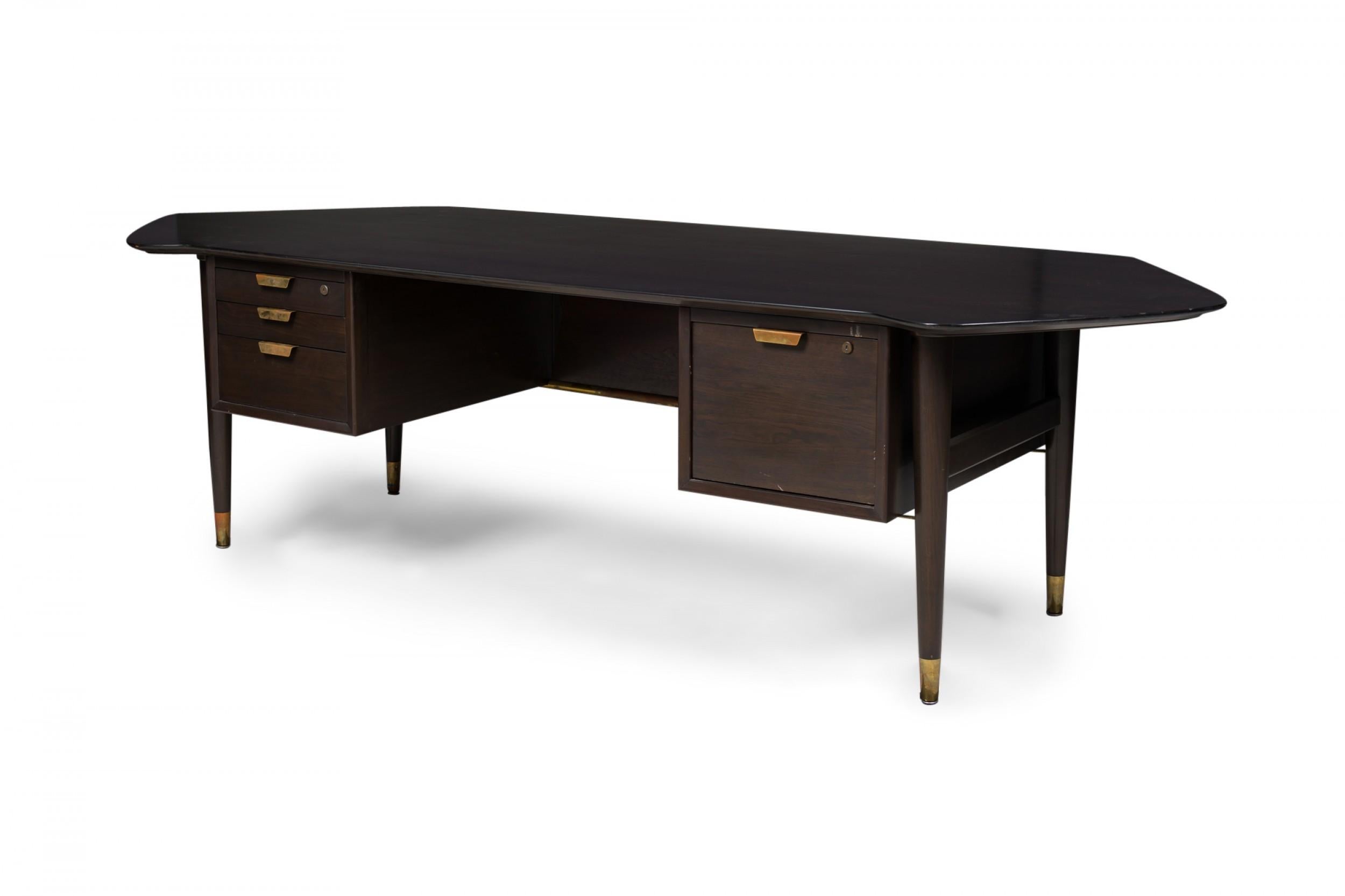 Contemporary Mid-Century-style dark wood veneer executive desk with an angular desktop supported by two column drawers with front privacy panel, resting on four tapered wood and brass legs. (STANDARD FURNITURE COMPANY, HERKIMER, NY).