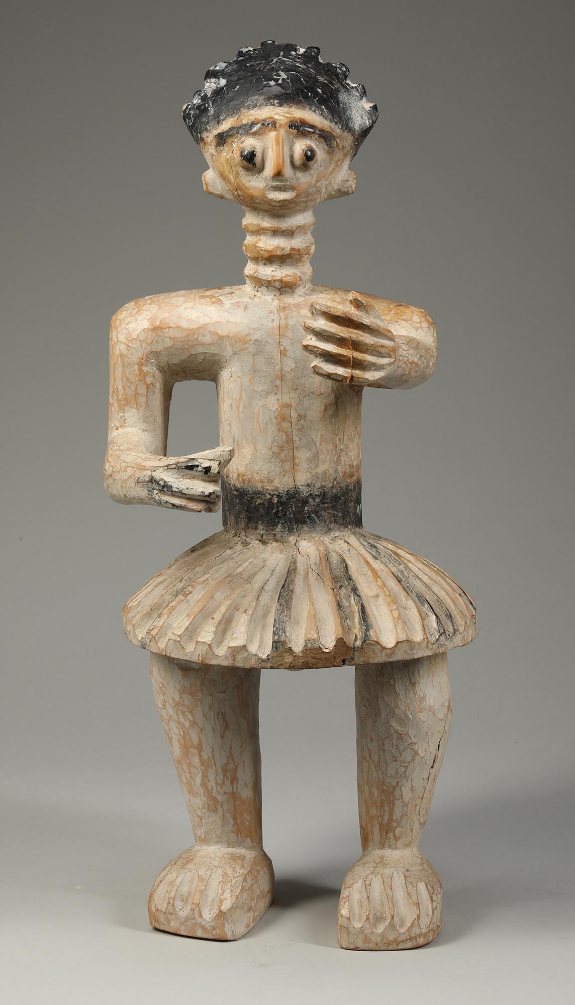 A Fante Drum Attendant standing male figure with flaring skirt and one arm out front. Bright open eye expression. From Ghana, early 20th century. As a display during traditional drumming performances and ceremonies in Ghana, carved wood figures are