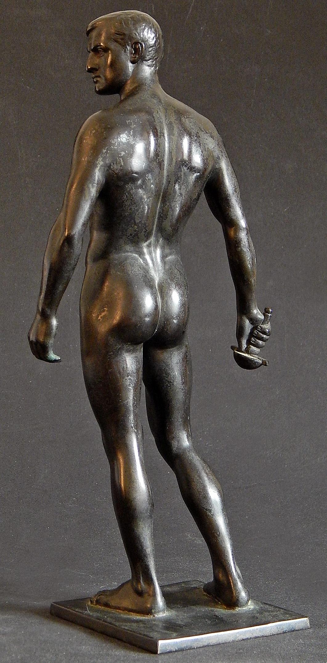 Beautifully modeled and detailed, this bronze sculpture of a nude male figure holding the hilt of a sword was created by Oscar Bodin, a German sculptor active in the early twentieth century (the figure is holding the hilt of the sword, but the blade