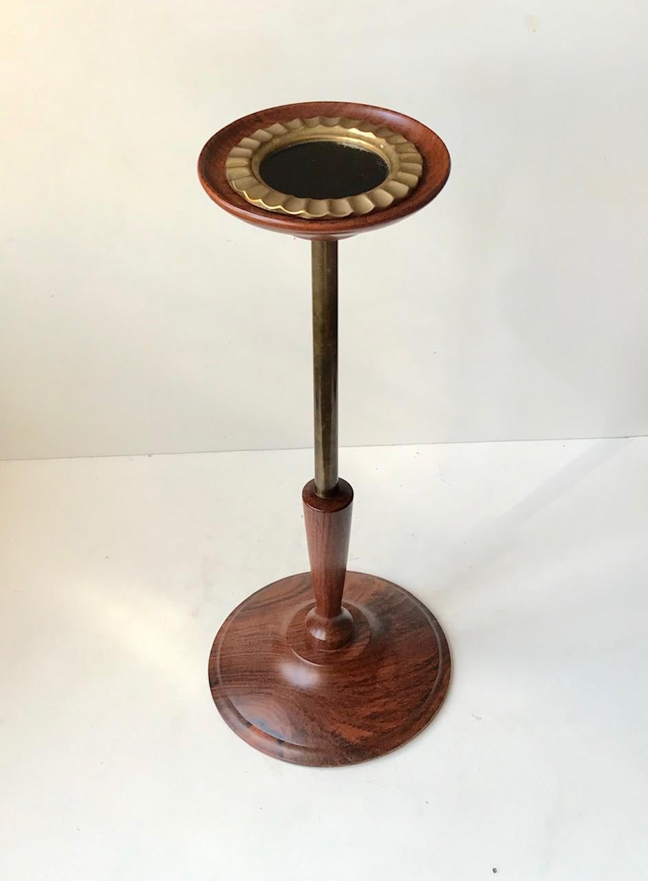 A freestanding ashtray fashioned from solid teak, exotic wood and patinated brass. It features a removable fluted ashtray in brass and black glass for easy cleaning. It was made in Denmark during the 1950s probably by Edmund Jørgensen. Measurements: