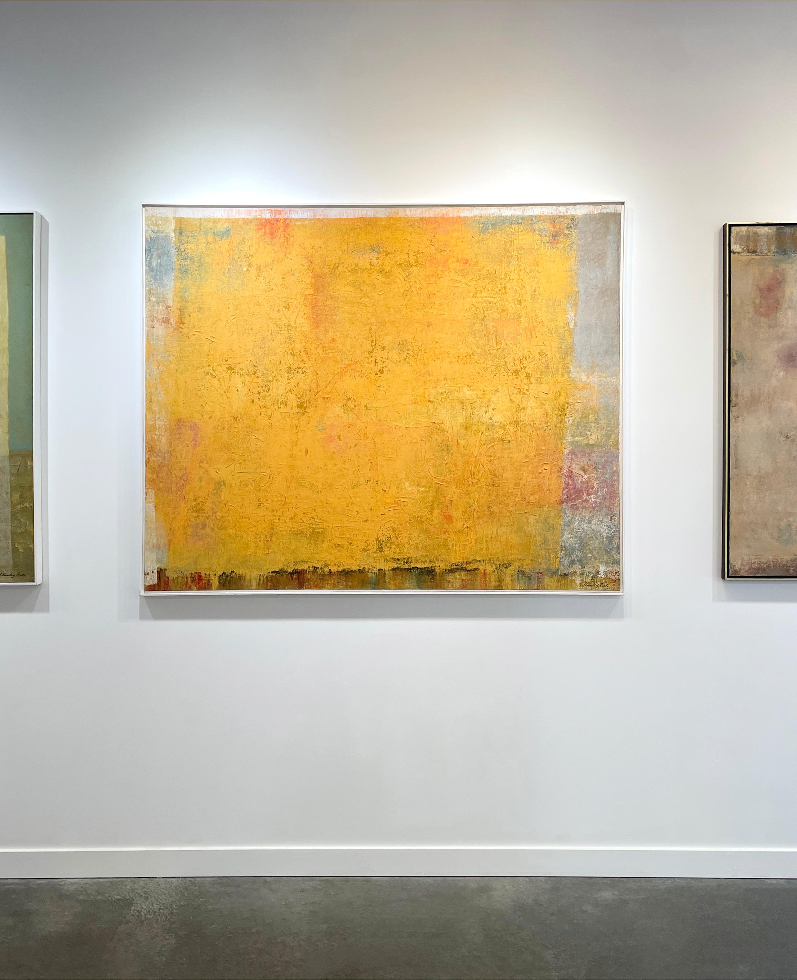 This original Modern abstract painting by Stanley Bate is made with oil paint on canvas. The artist has layered different muted colors like grey and maroon beneath a vibrant yellow layer of paint. The result is a bright, warm, highly textured piece.