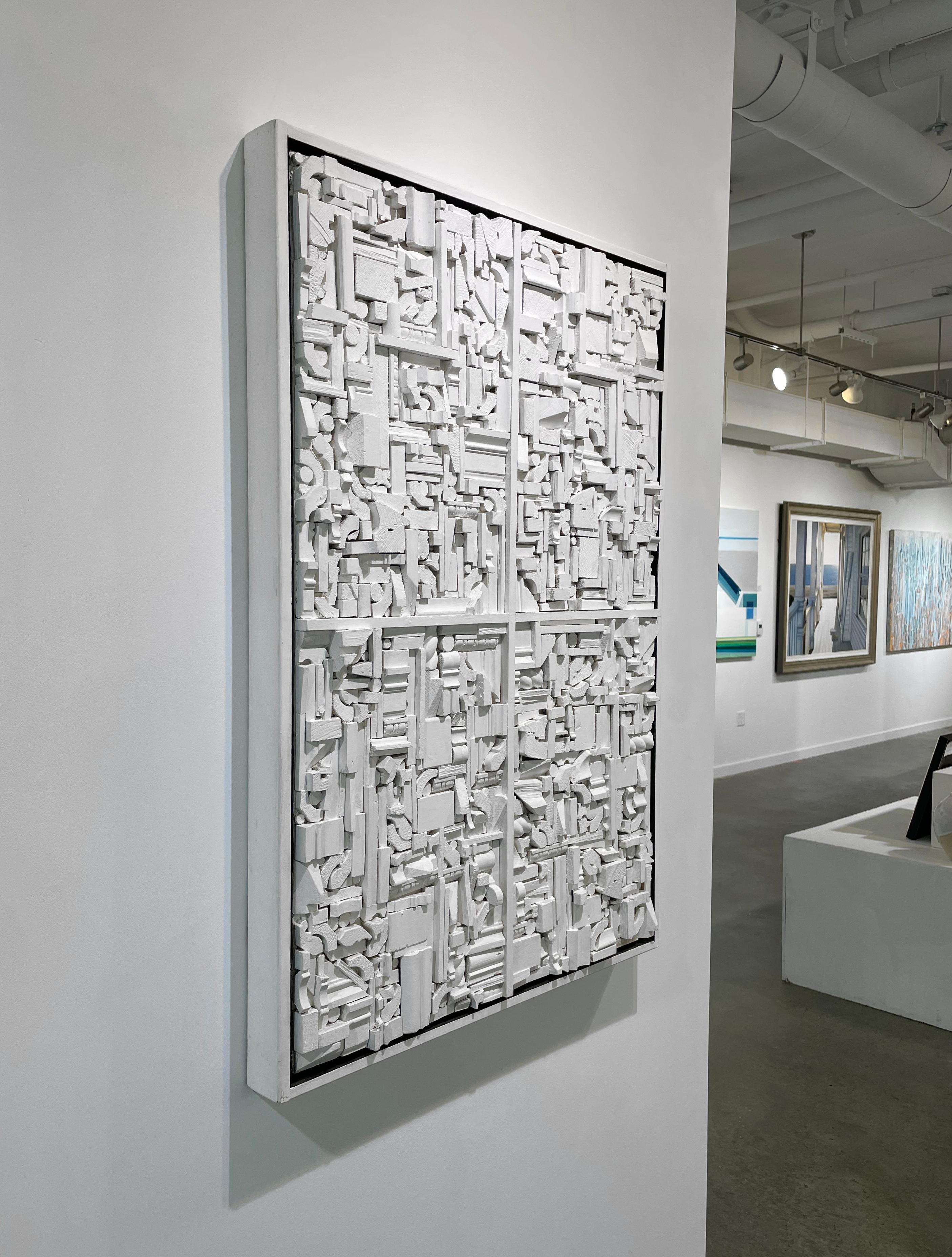 Questo pezzo astratto moderno di Stanley Bate è una scultura in legno dipinta di bianco. I pezzi tridimensionali che ricordano i pezzi architettonici sono strettamente impilati l'uno con l'altro per creare un pezzo geometrico. Un pezzo di legno