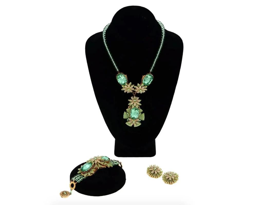A vintage three-piece jewelry set by Stanley Hagler. The set includes a necklace, a bracelet, and a pair of clip-on earrings. The pieces are made of green and beige beads and crystals with golden fittings. Each item is marked Stanley Hagler NYC on