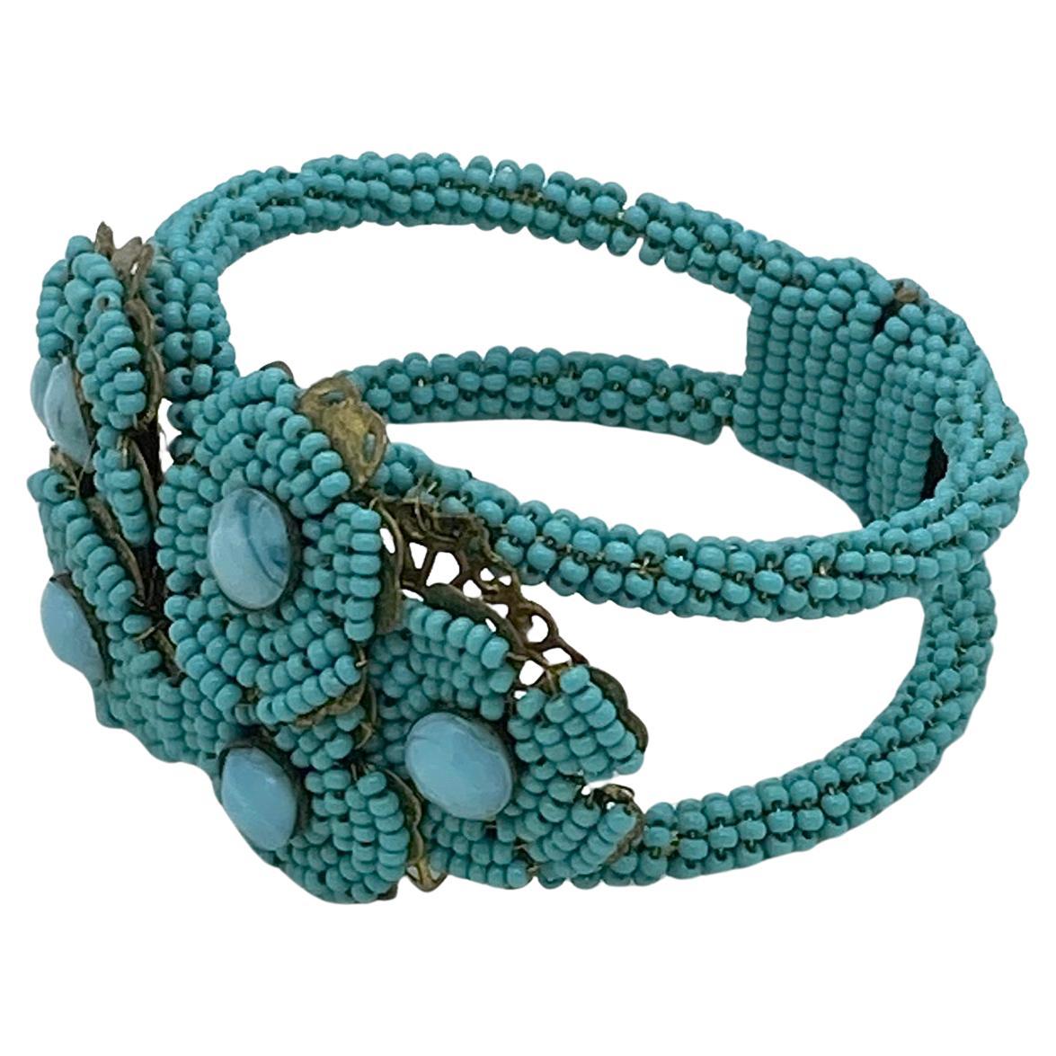 This is a Stanley Hagler hinge clamp bracelet. It is wrapped around with turquoise color seed beads and features six hand wired flowers on brass filigree. It's very similar to Stanley Hagler's beading style but is not signed.

Our vintage jewelry