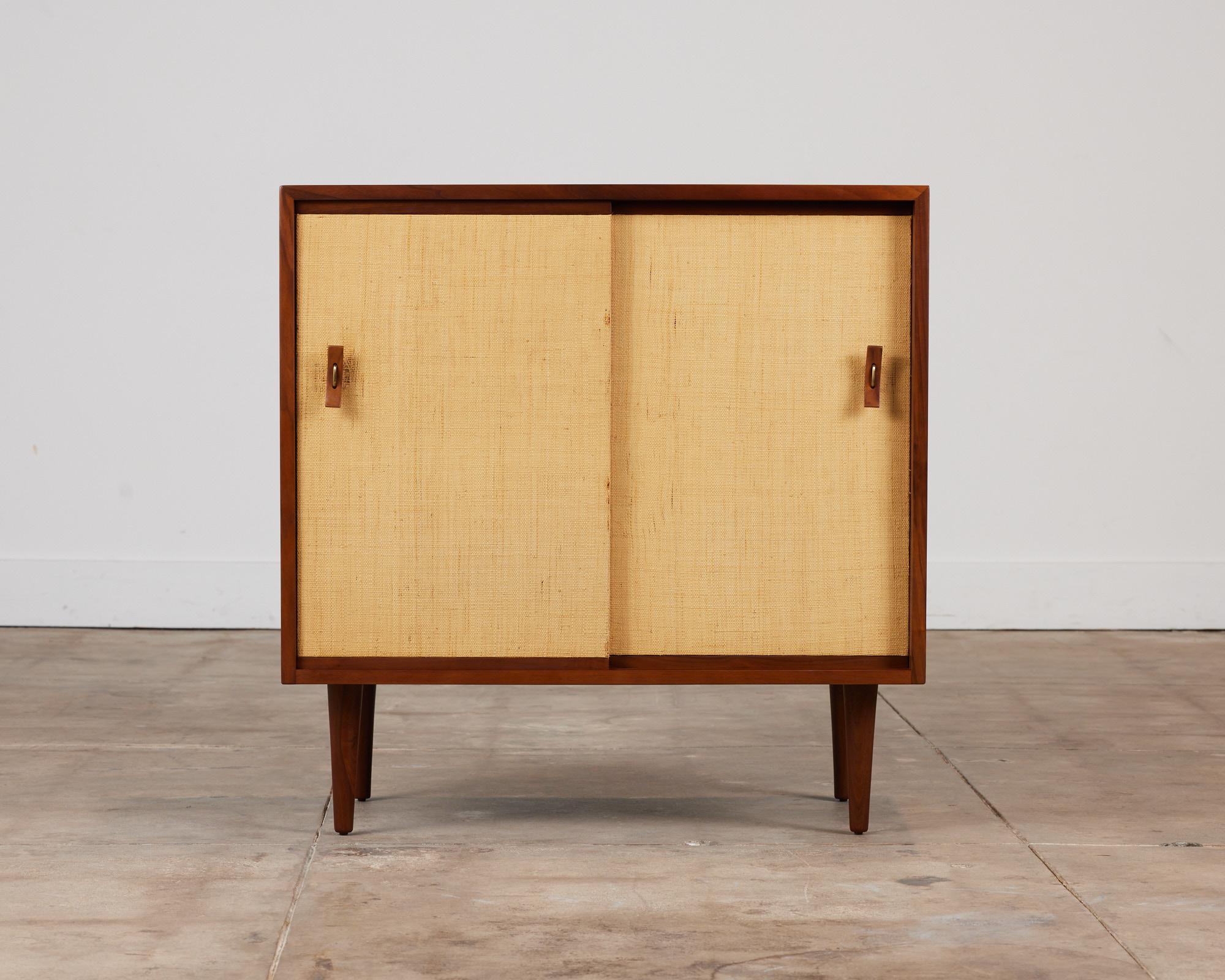Stanley Young for Glenn of California grass cloth door credenza, c.1950's, USA. This walnut piece features Young's trademark bentwood and brass pulls. The two sliding door are finished with grass cloth fronts. Inside, you can find one shelf for