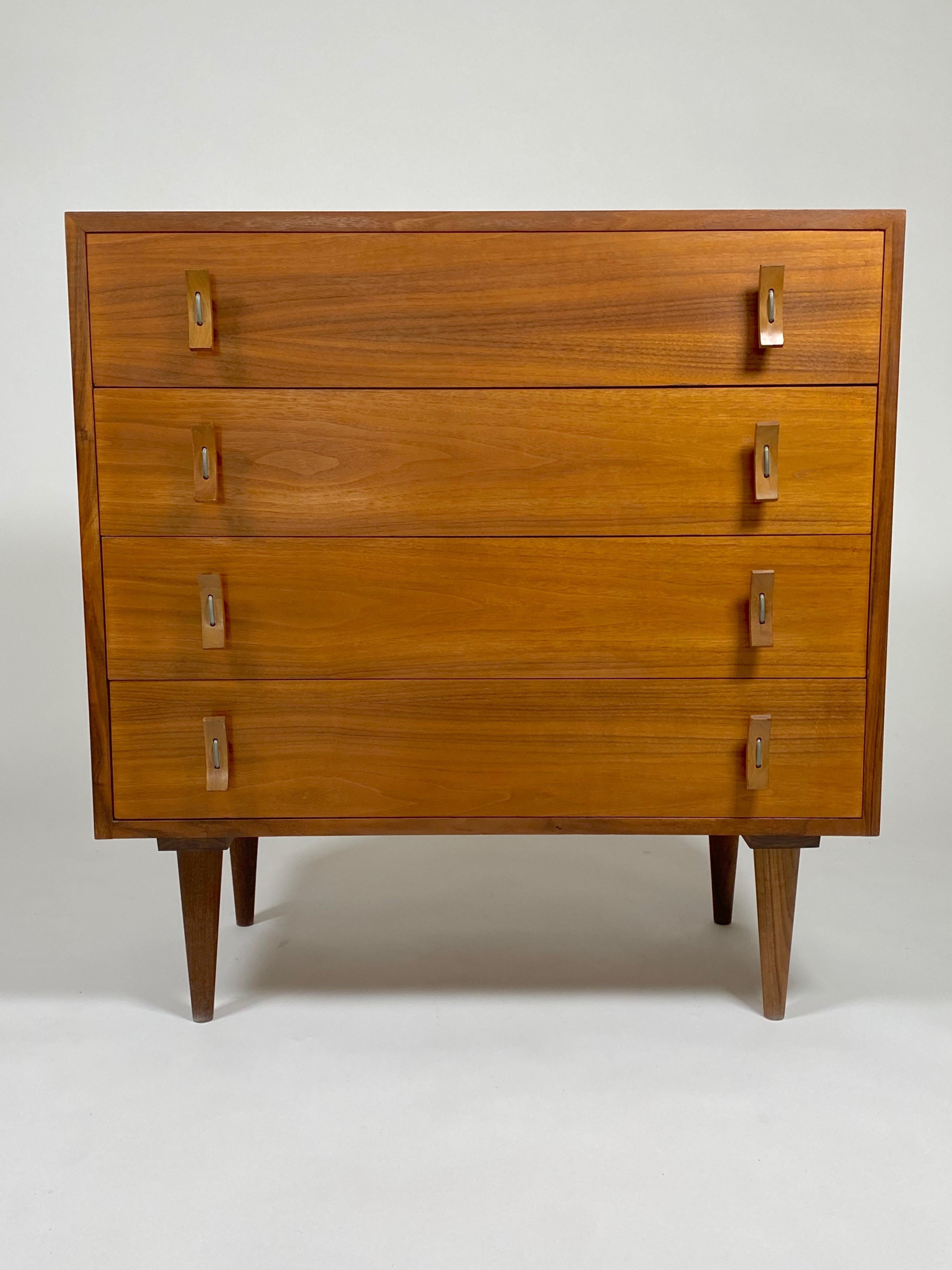 Post War Design compact four drawer dresser in California walnut by designer Stanley Young for Glenn of California. Curved wooden pulls held in place by cuvred aluminum fasteners. Resting on tapered dowel legs, the cabinet is richly colored and