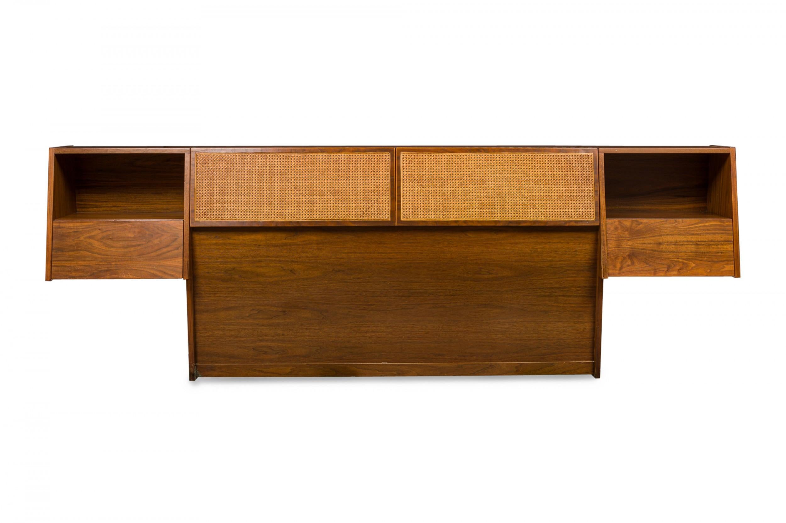 American mid-century queen-size bed headboard with a walnut case featuring two open cabinets on the outermost sides with a drawer beneath each, and two caned center panels that open to reveal two interior compartments. (STANLEY YOUNG FOR GLENN OF