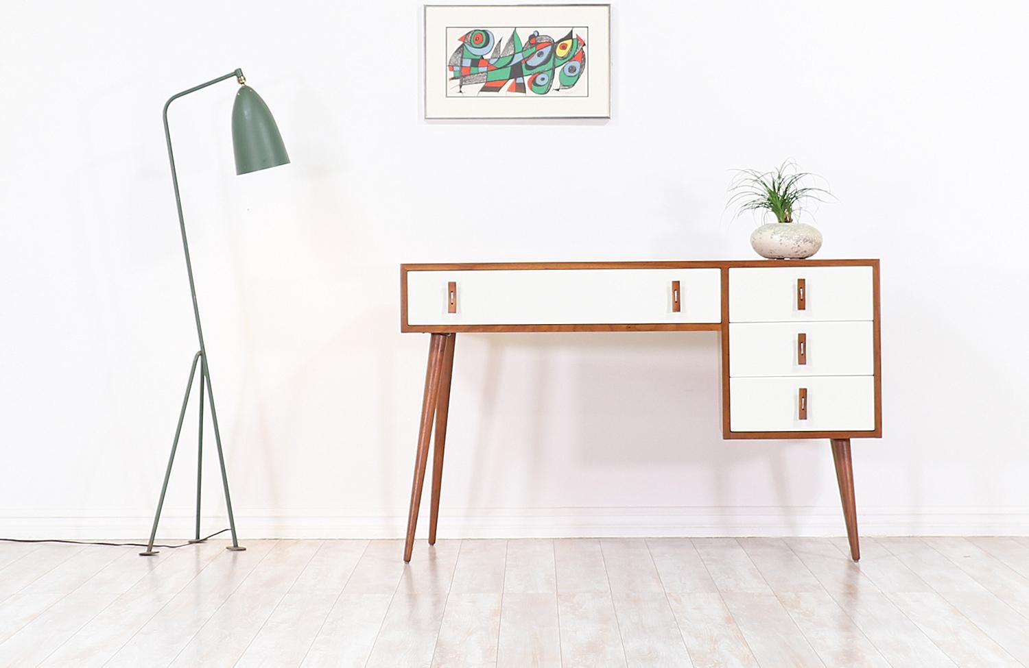 Stylish modern writing desk designed by Stanley Young for Glenn of California in the United States, circa 1950s. This striking design features a walnut wood frame sitting on angled tapered legs, with white lacquered front detailing and intricate