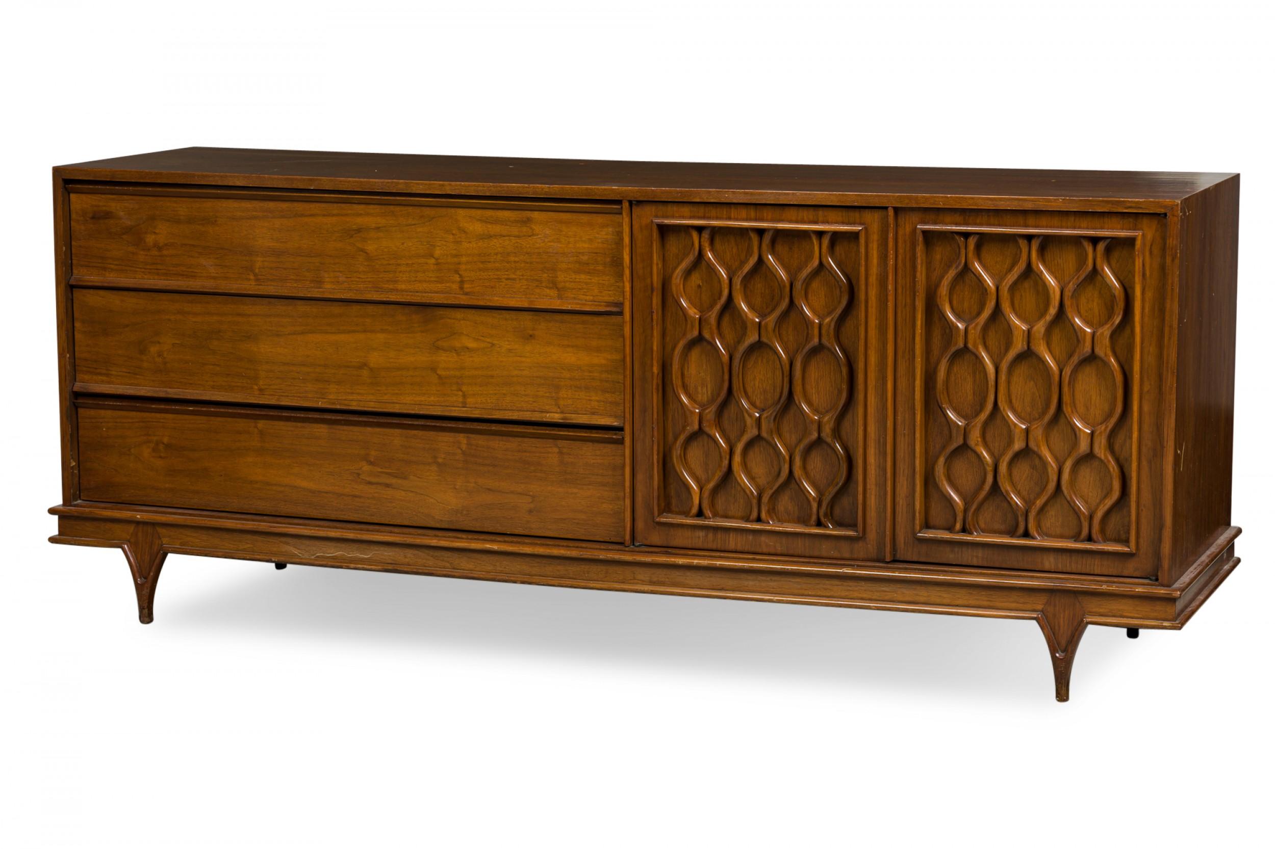 American Mid-Century walnut credenza / sideboard with three drawers on the left side, and two cabinet doors on the right with decoratively carved geometric fronts, resting on four short tapered walnut legs. (STANLEY FURNITURE).