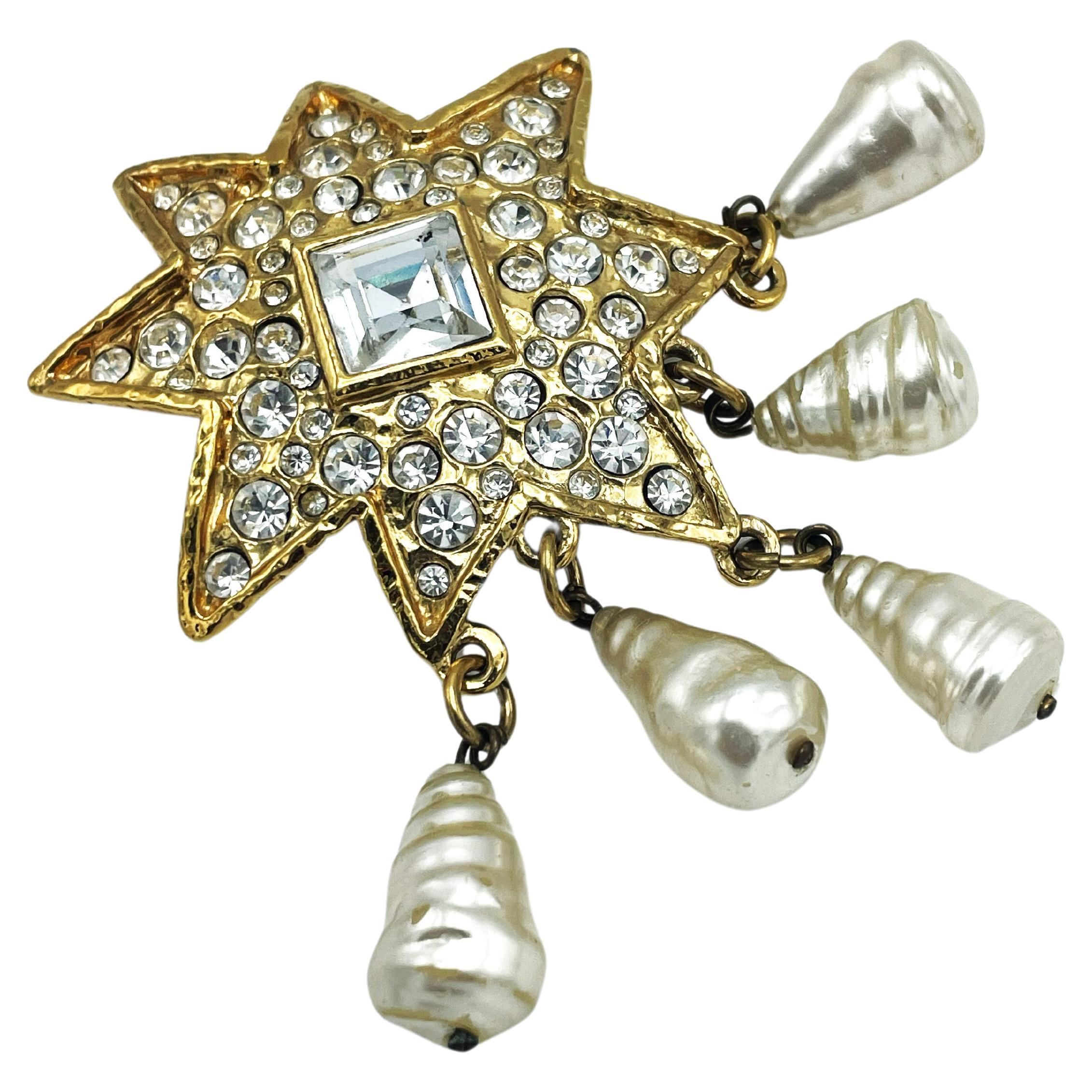 
CHRISTIAN LACROIX STAR BROOCH (Made in France) vollständig mit Strasssteinen besetzt.
In der Mitte befindet sich ein großer, quadratischer Strassstein mit den Maßen 1,5 x 1,5 cm. 

Abmessungen:  Stern 5 x 5 cm, Perlen 2,4 cm x 1,2 cm, Gesamtlänge 9