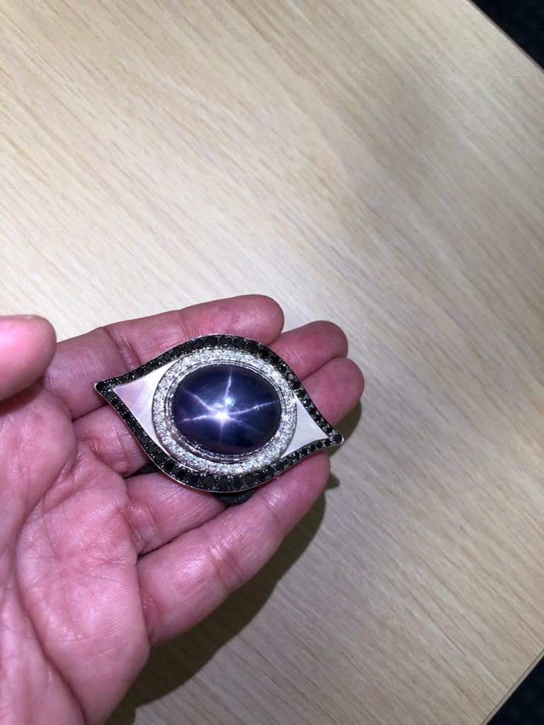 A divine 18k white gold pendant necklace shaped as an eye, centering a star sapphire weighing approximately 79.55 carats crafted within a frame of brilliant white diamonds weighing 1.20 carats. The pendant is further extended by mother of pearl