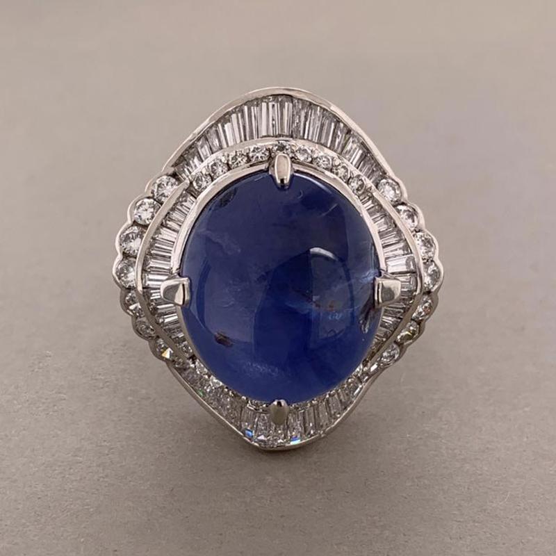 A large 26.45 carat star sapphire takes center stage in this bold cocktail ring. The blue sapphire displays asterism which is the term for a 6 ray star when a light is flashed on the top of the gemstone. It is accented by 2.15 carats of round