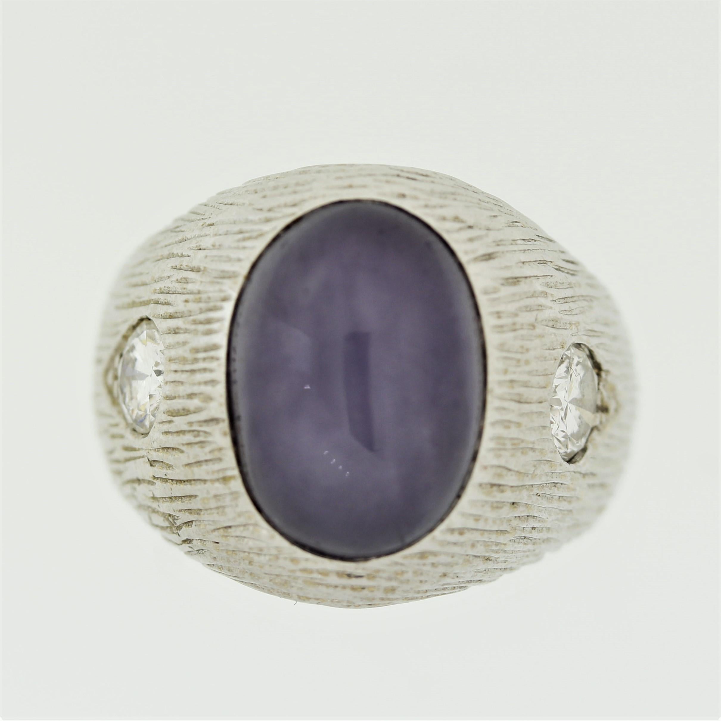 A simple yet stylish men’s ring featuring an approximately 19.70 carat natural star sapphire. It has a pleasing purple-blue color with a prominent star and is free of any treatments. It is accented by two large round brilliant-cut diamonds weighing
