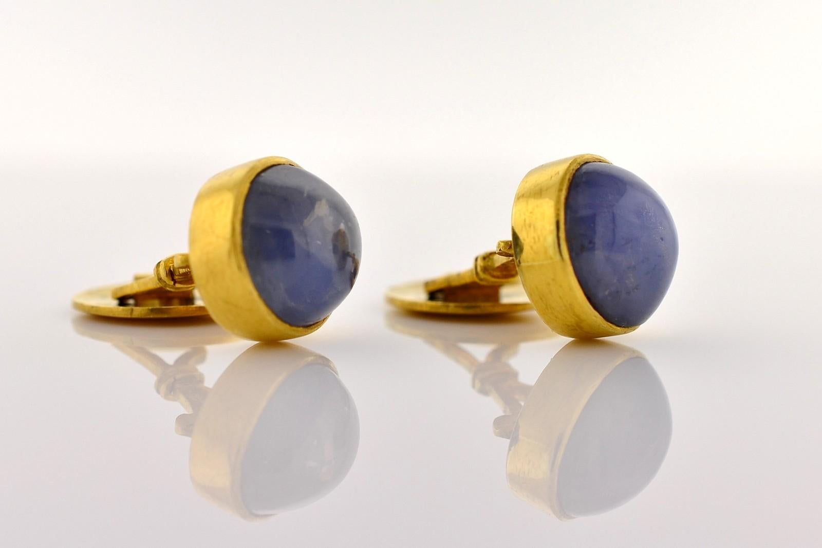 These one-of-a-kind cuff links feature two cabochon Ceylon Star Sapphires.   The Sapphires are bezel set in 18KT yellow gold and both total approx. 20 carat.  One Sapphire measures 13.25 x 11.30 x 7.40 mm and the second measures 12.60 x 11.45 x 7.20