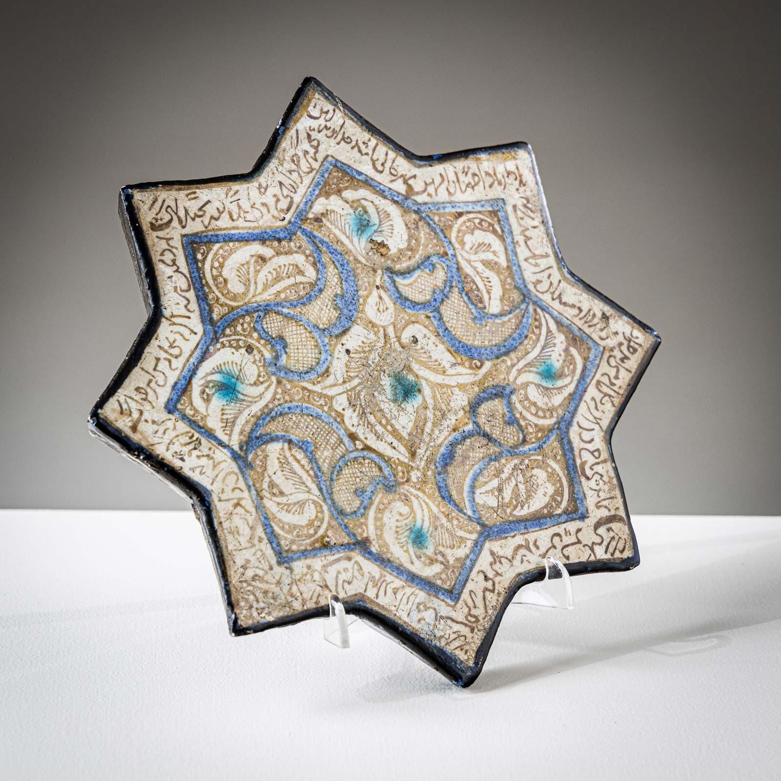 Piastrella in ceramica a forma di stella a otto punte con decorazione beige-blu e scritte circostanti. 