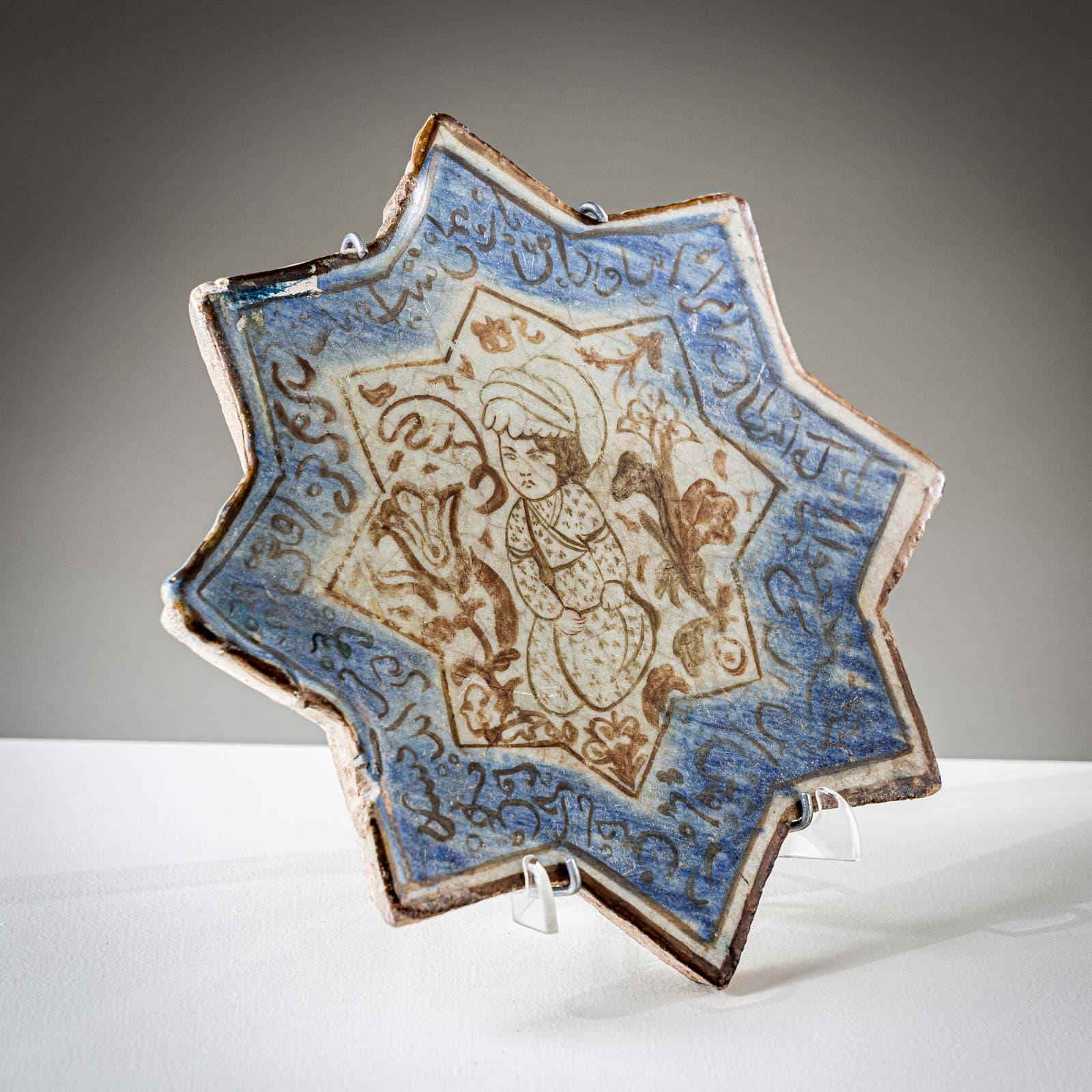 Mattonella in ceramica a forma di stella a otto punte con decorazione marrone-blu e raffigurazione figurativa al centro e scritte circostanti. 