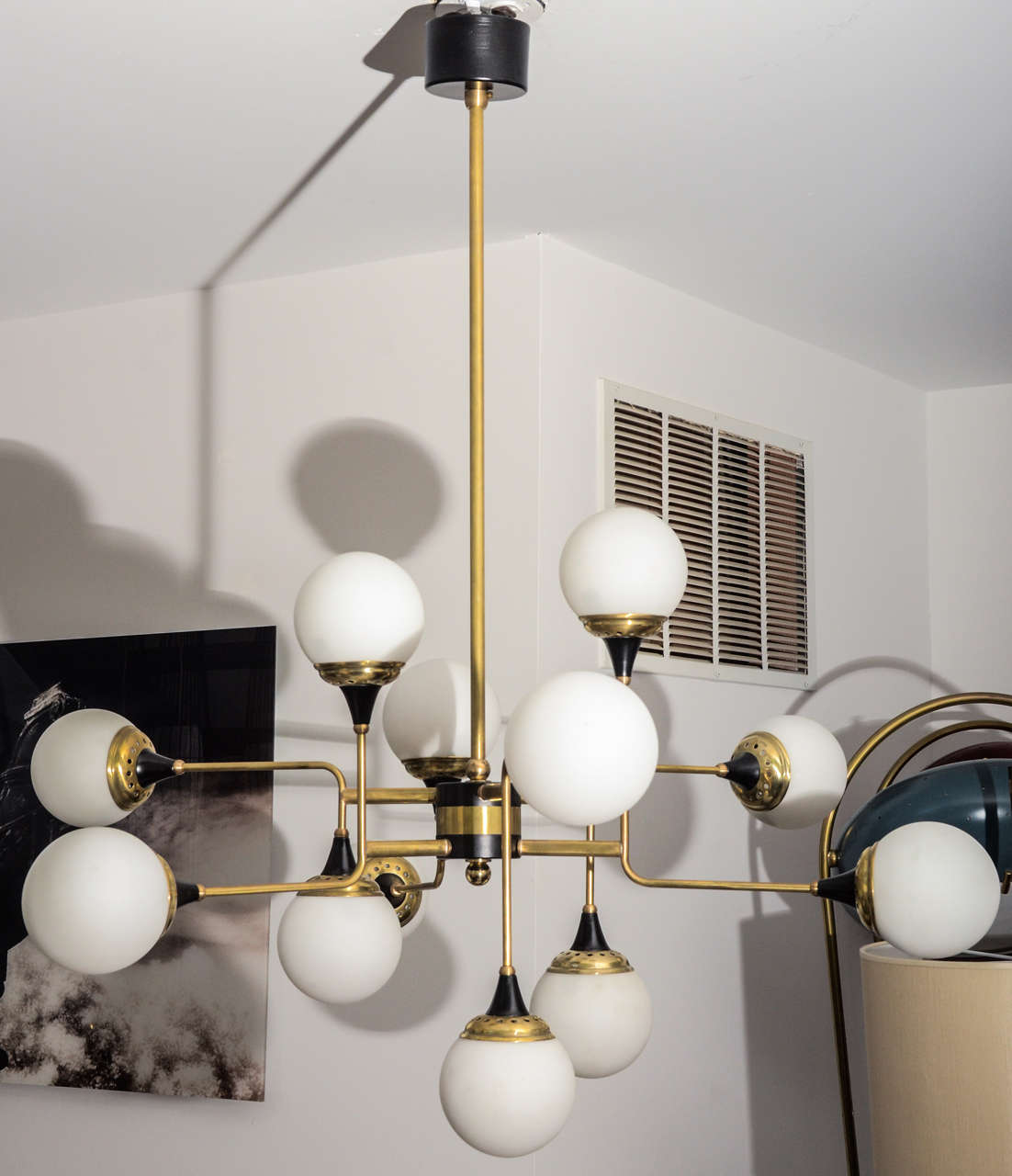 
An asymmetric shaped chandelier composed by six bent brass arms with black enamel details in the style of Stilnovo mid-century.  12 hand blown white glass globes made in Italy.