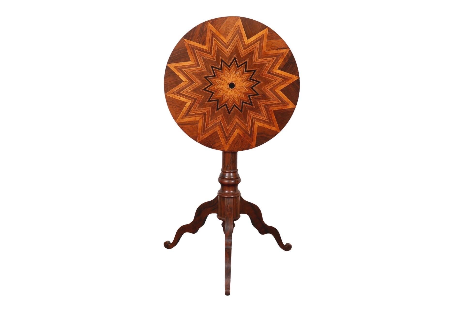 A round fruitwood tilt top occasional table. The top is inlaid with a parquetry sunburst design in rose wood, ebony and maple veneers. The tilt mechanism is cast iron and no longer has the pin to adjust the height of the table top. The base consists