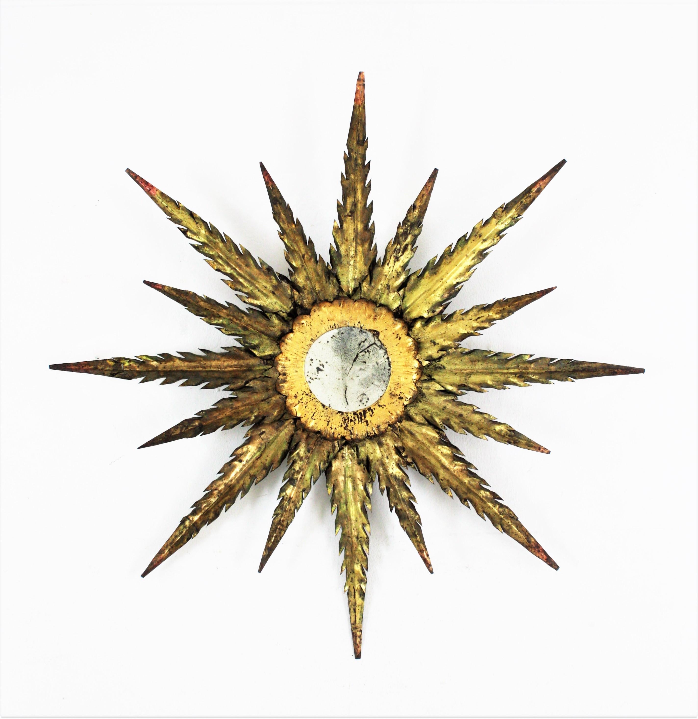 Rare handcrafted parcel-gilt iron sunburst / starburst shaped wall mirror, Spain, 1940s-1950s.
This Brutalist mirror has two layers of rays in different sizes with jagged pointed edges. It has a terrific aged patina gold leaf finish and green