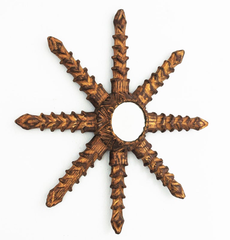 A beautiful carved giltwood starburst wall mirror, Spain, 1950s-1960s.
This hand carved star shaped sunburst mirror has an unusual design with thick jagged rays.
Carved wood patinated in gilded color.
Interesting to be placed alone or in a wall