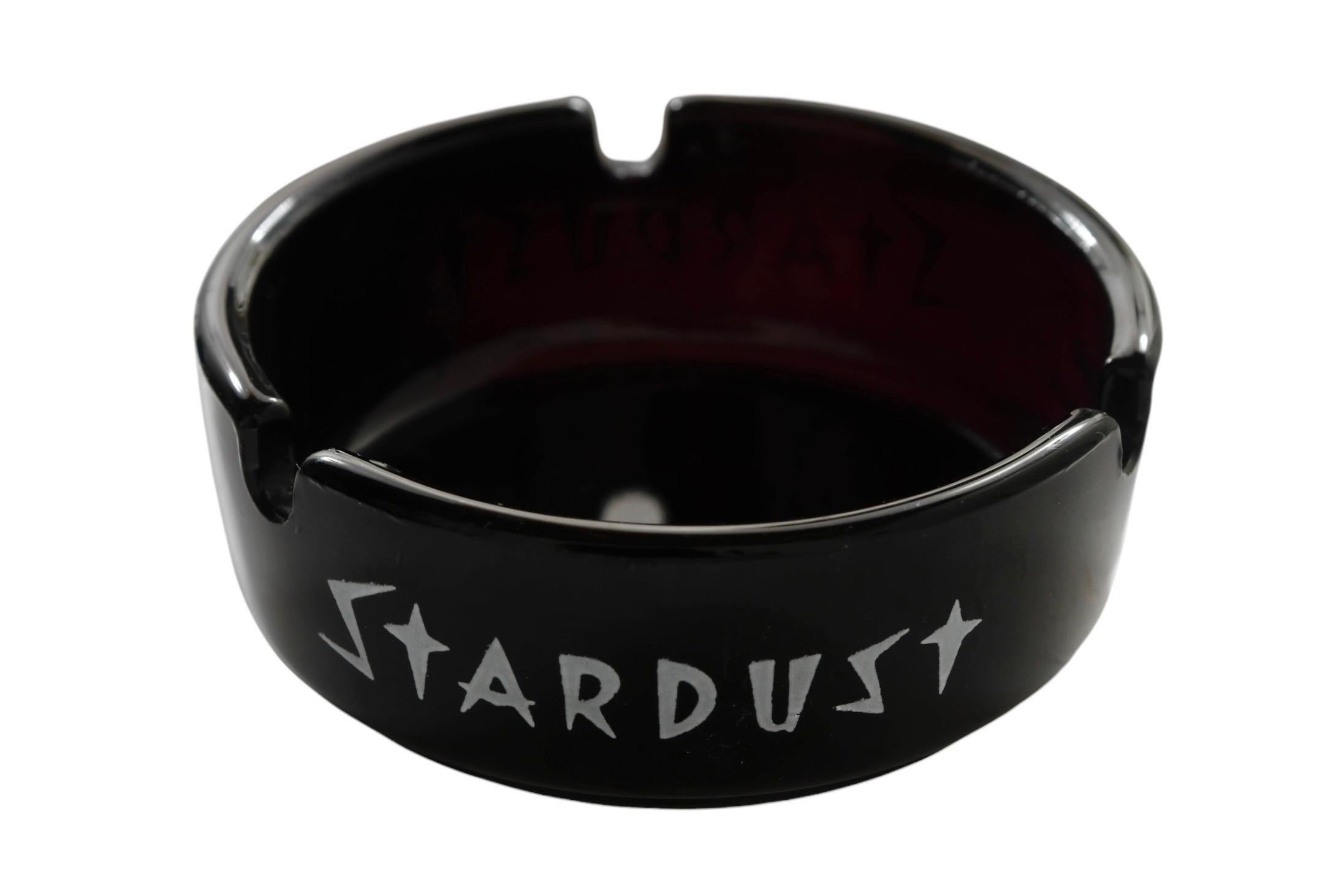 A black glass ashtray from the Stardust Hotel & Casino in Las Vegas, Nevada. Printed around the edge in white with the Stardust logo.

