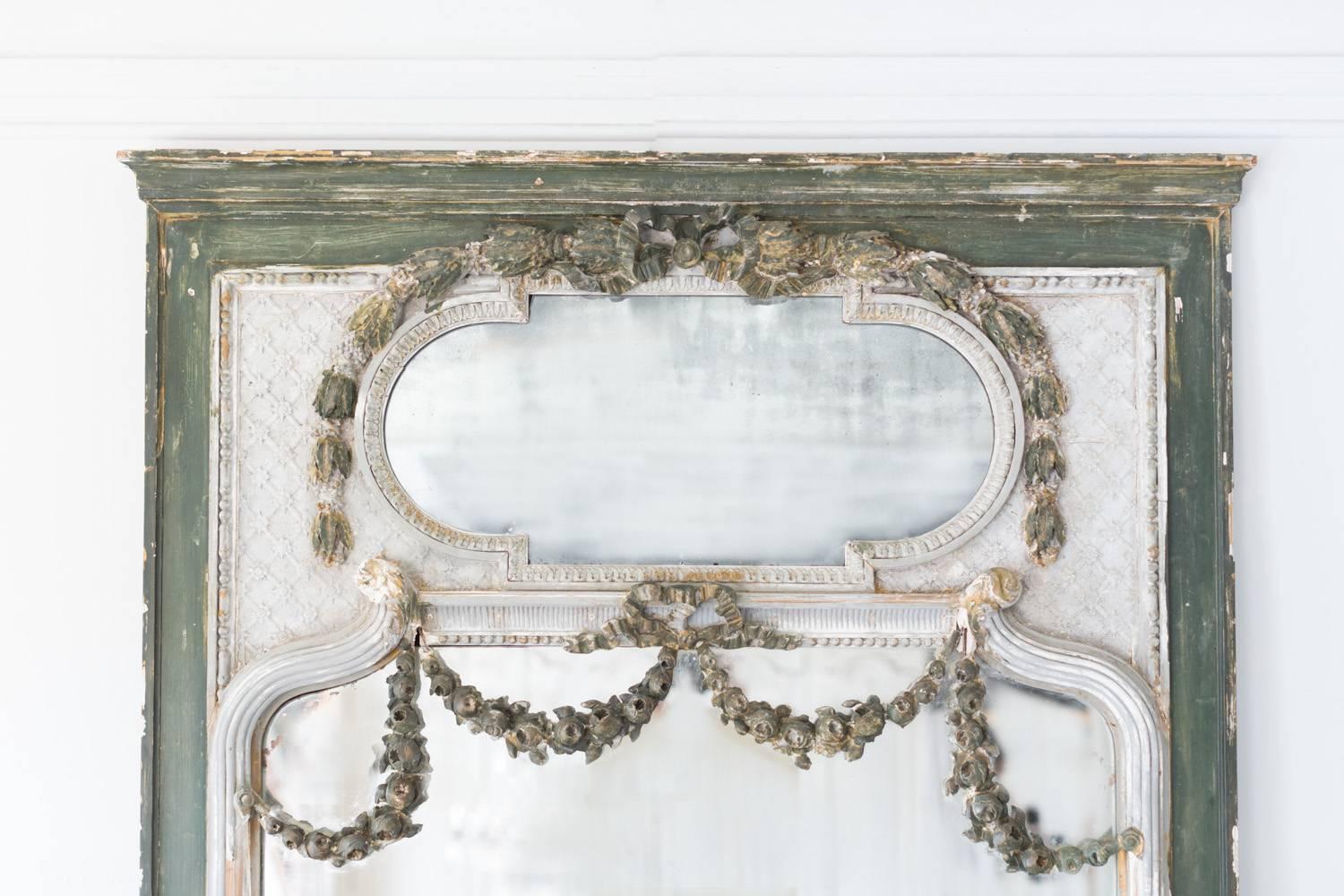 Antique Louis XVI mirror in distressed silver and kelly green finish. A sweet rose garland spills over the main glass, another string of flowers frames the top of the oval glass. The main mirror boasts a small crack in the middle and gradient