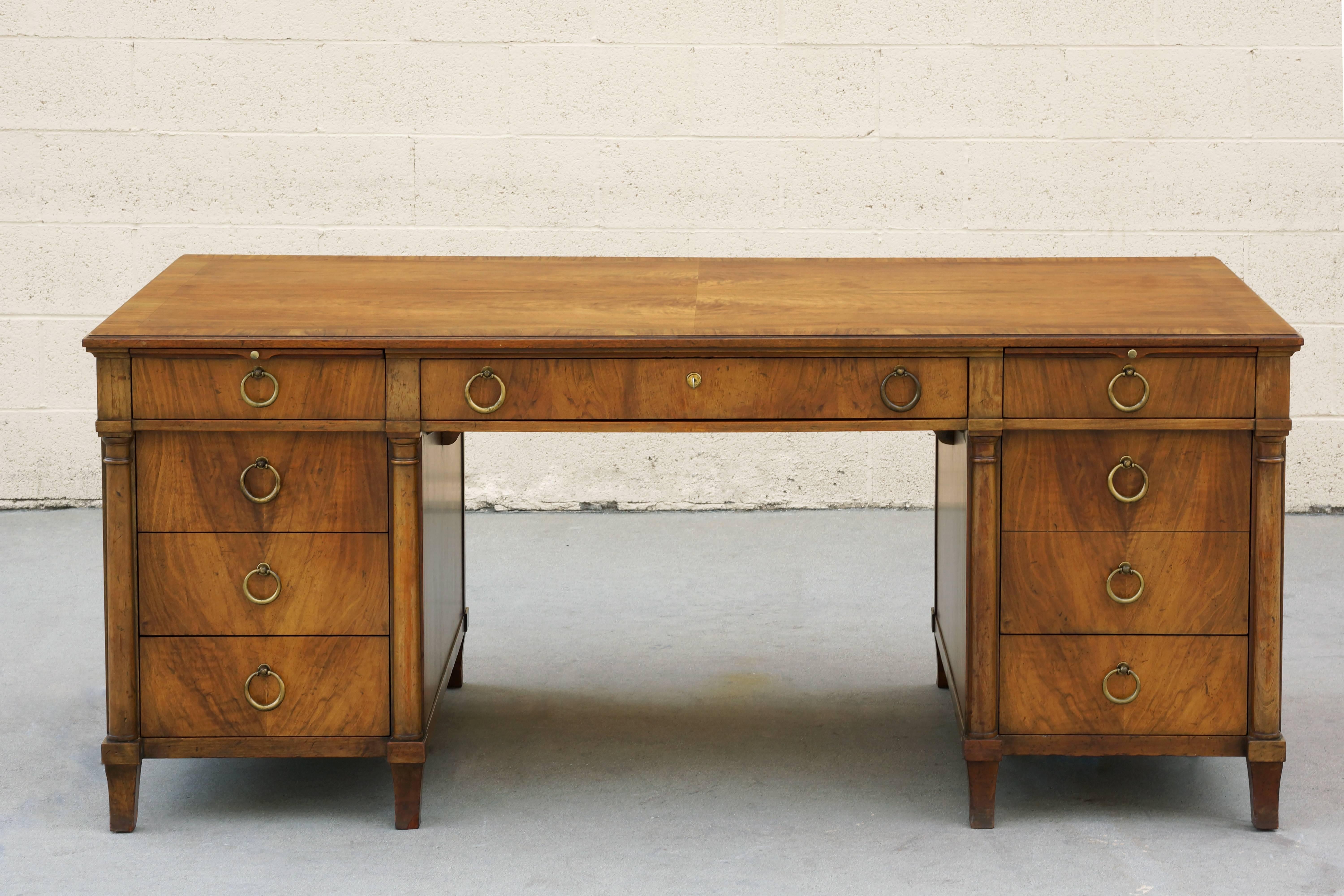 Classic American Empire executive desk by Baker. This impressive solid walnut desk features six legs, brass pull rings, pull out paper trays and locking utility drawer with key. Most uniquely, the front of the desk includes a large pull out wood