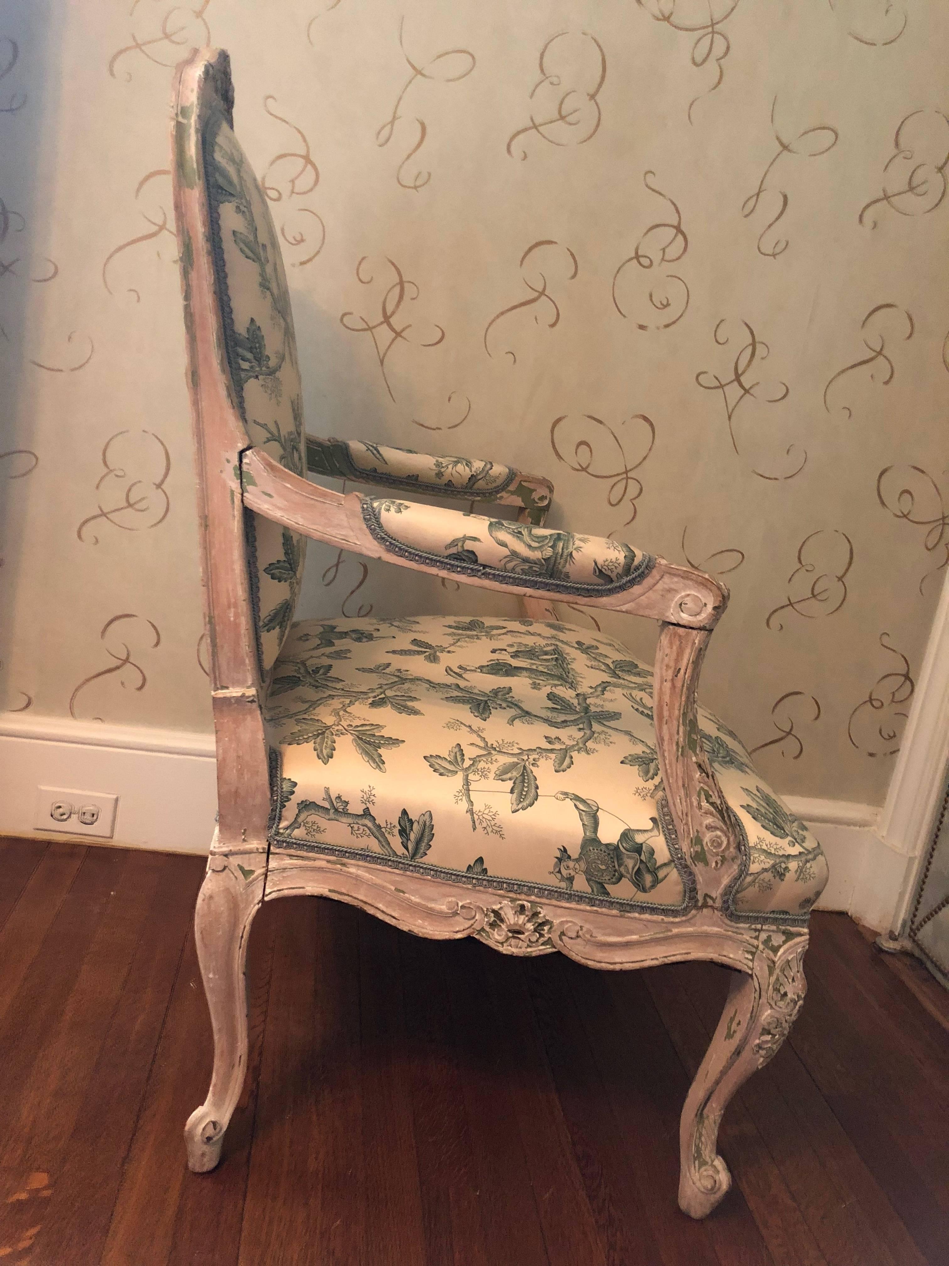 Gorgeous Louis XVI style chair upholstered in a designer chinoiserie motif silk fabric. The chair has remnants of a blue/green paint appearing on the wood, contributing to its overall character. Measure: Arm height is 27, apron to floor is 11.5.