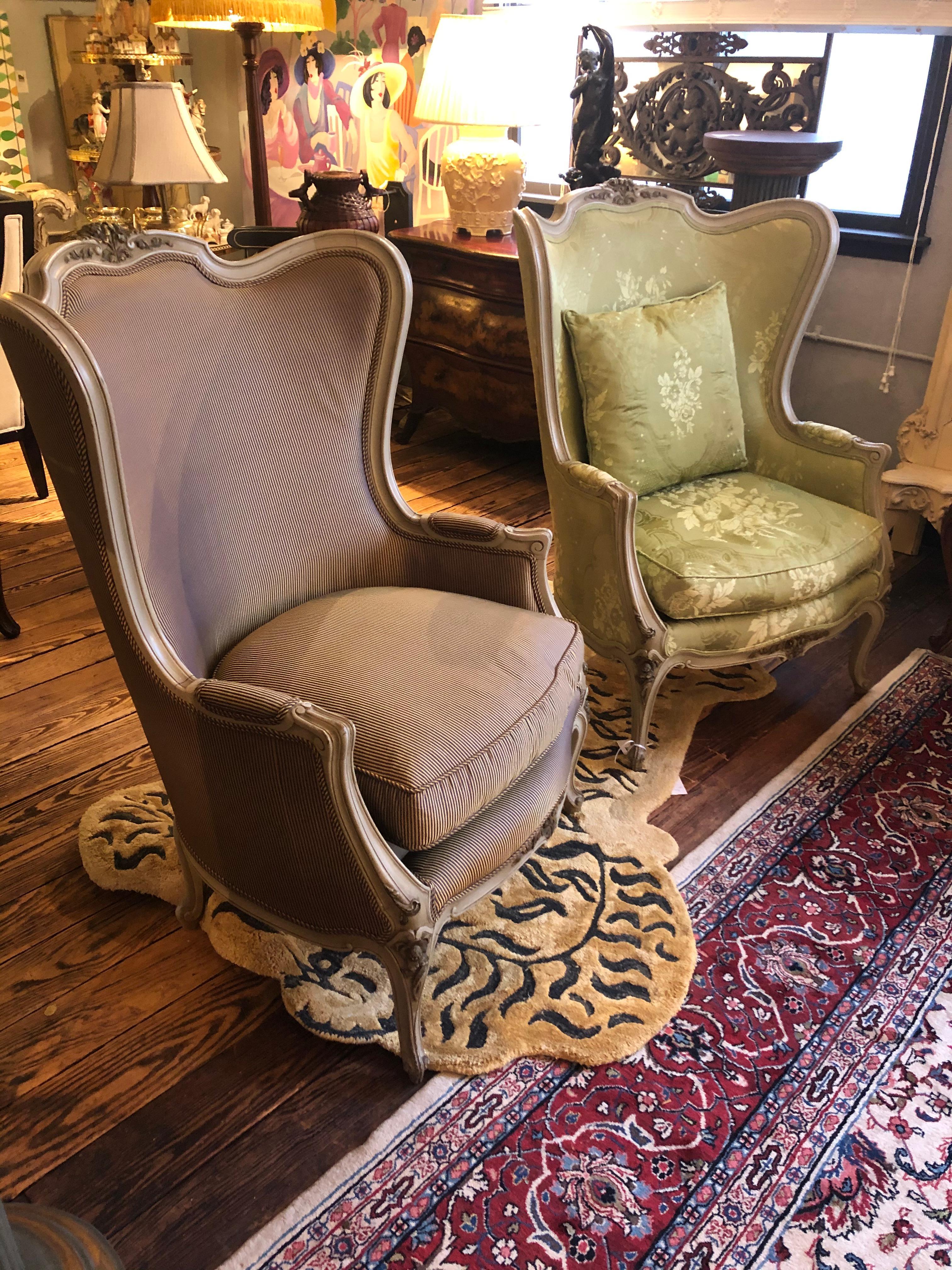 An impressive elegant pair of French Louis XV style cream painted and gilded carved beechwood bergeres having ormolu decoration and each sumptuously upholstered in silk. One chair is a pale green damask, the other a navy and gold stripe. Down