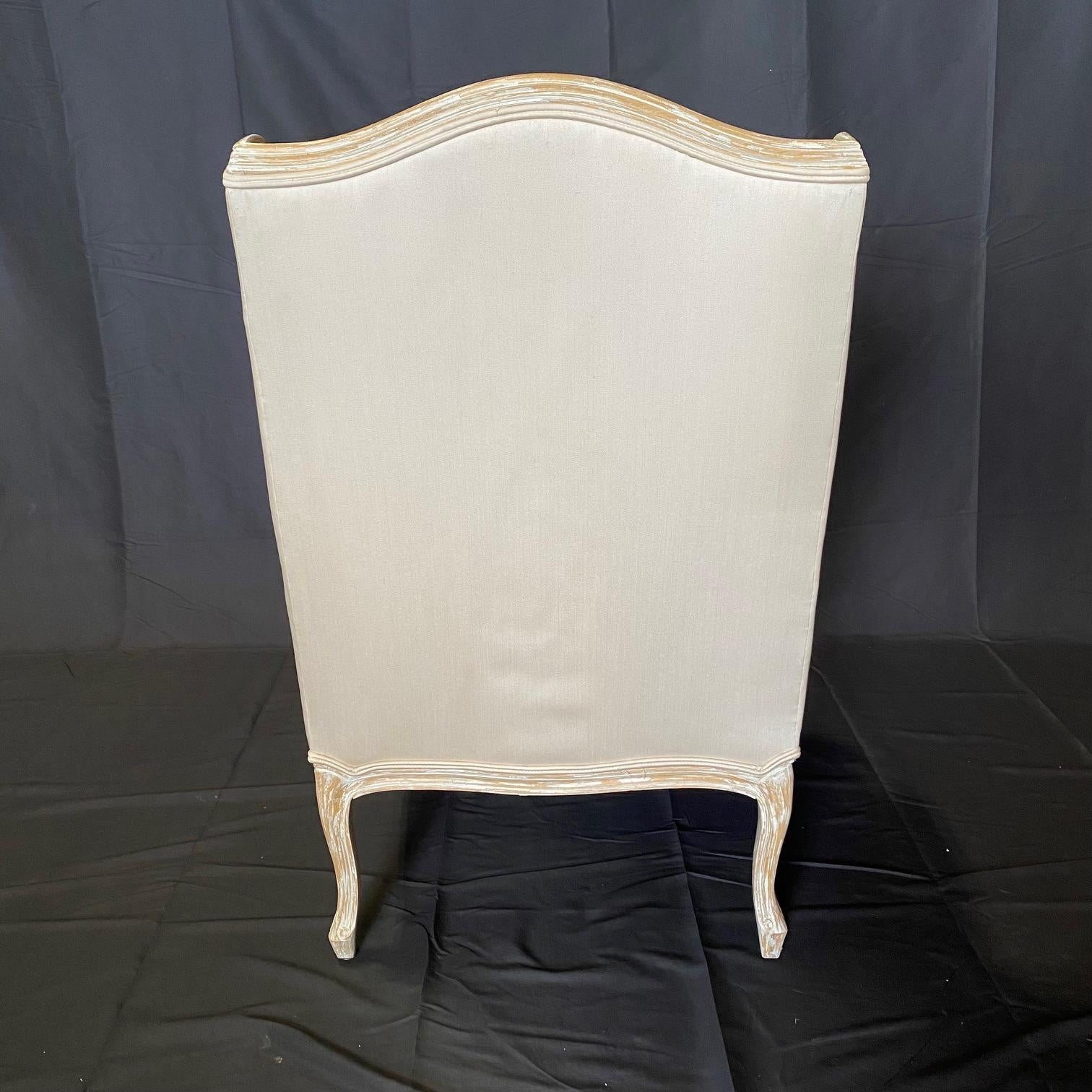 In the style of Louis XV, this pair of French lounge chairs with wing back details have wonderful patina on their frames: patinated wood. These elegant chairs have been upholstered in a pale white linen/satin blend. arm height 23.25
#6126